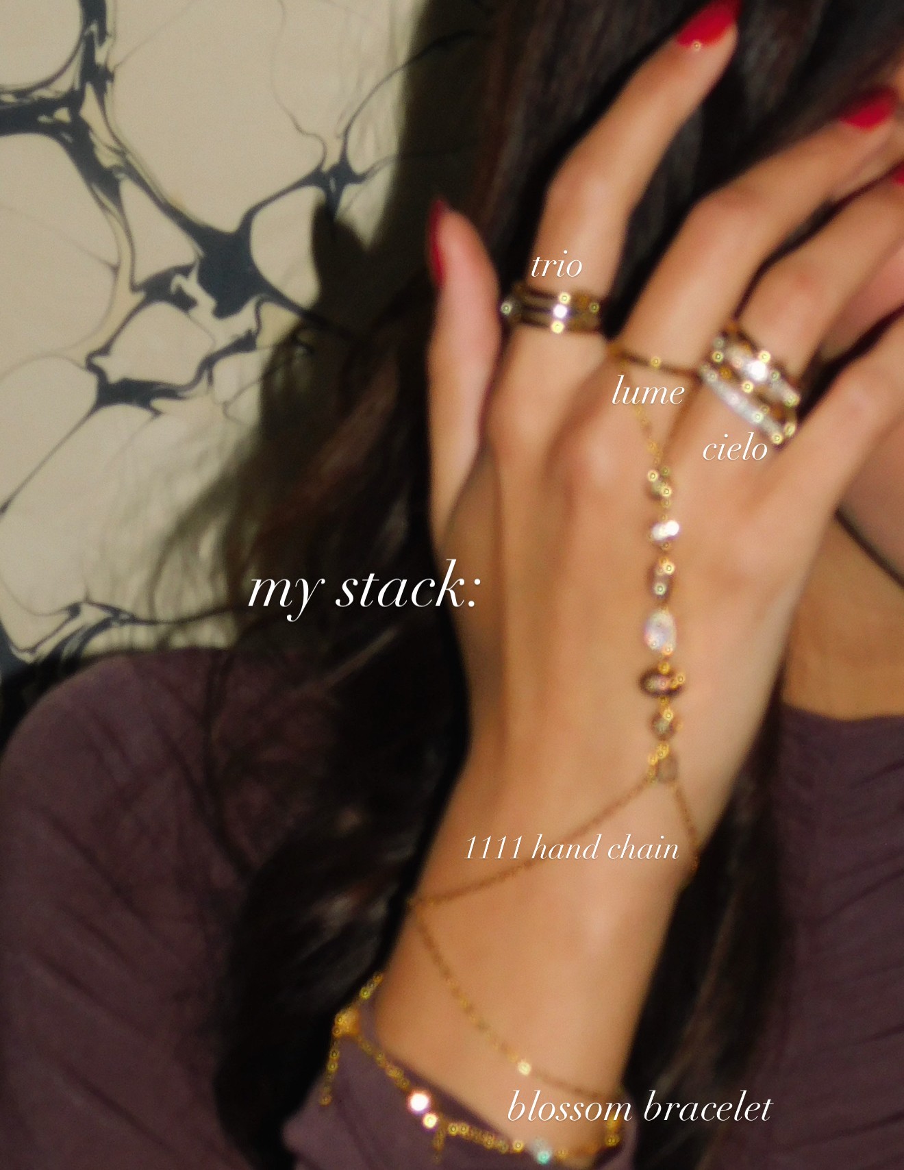 Close-up of a woman's hand with rings, a chain, and a bracelet, against a patterned background.