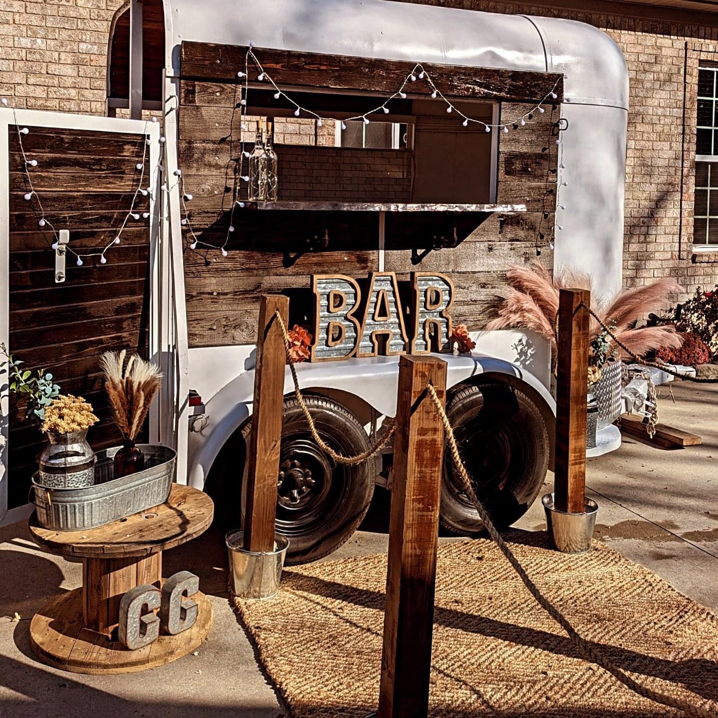 Bar setup with speakers, wooden sign, and decorative items outdoors on a mat.