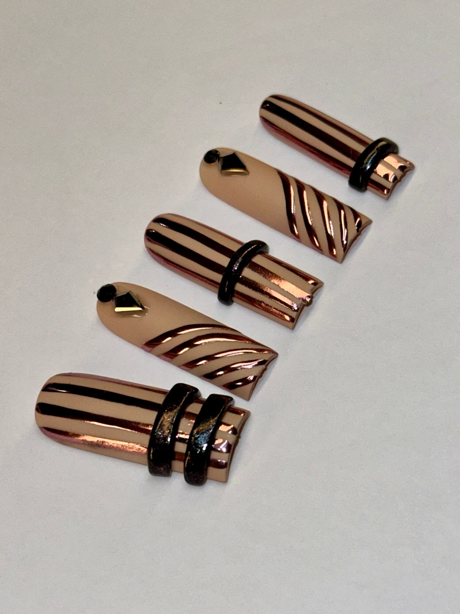 Four rose gold lipstick cases with black bands arranged diagonally on a white surface.