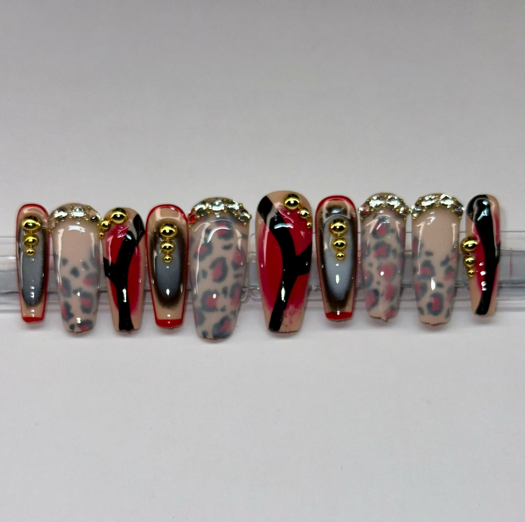 Nail art with leopard print, red, black, gray, and gold accents on artificial nails.