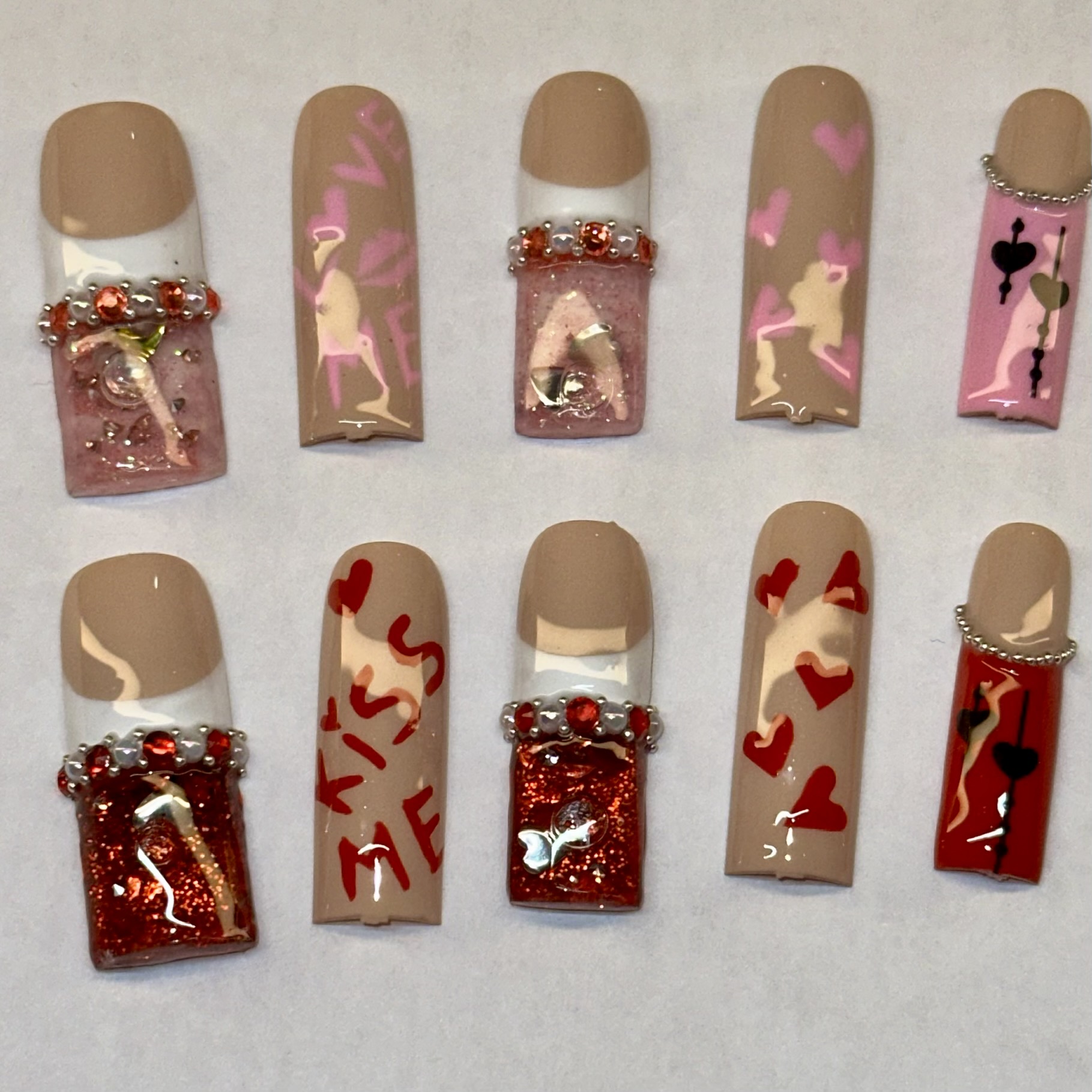 Nail art with pink and red designs, including hearts, reindeer, and glitter, on beige base nails.