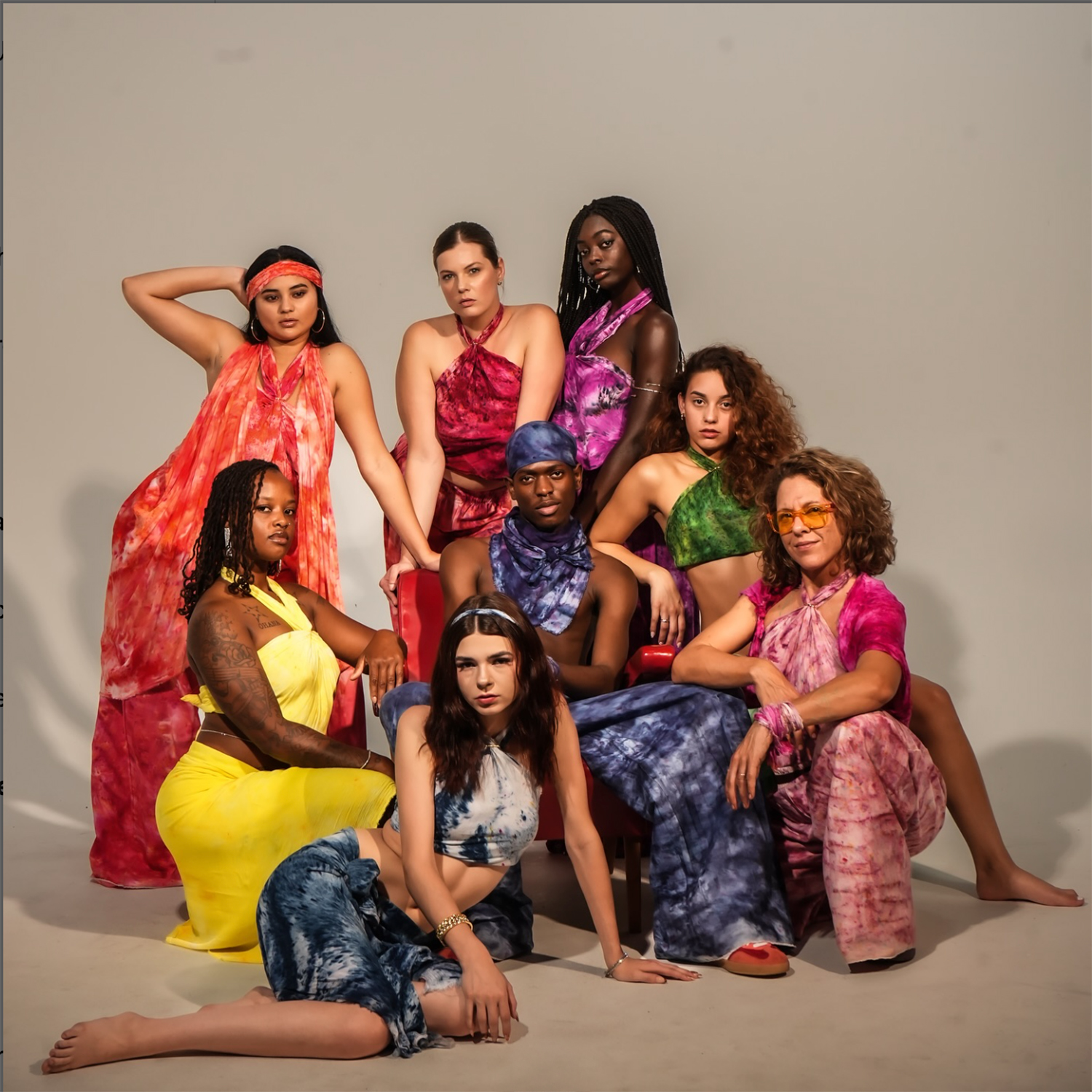 Group of nine women in colorful dresses posing against a plain background.