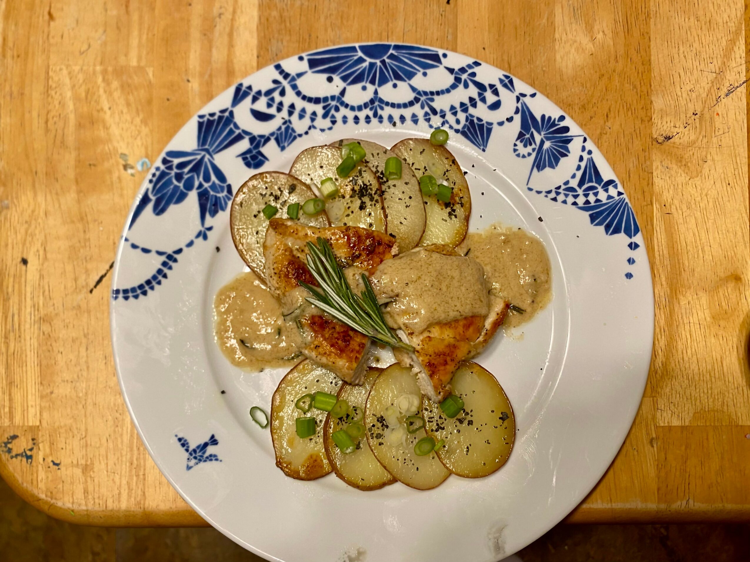 Plate with roasted potatoes, chicken, and green herbs on a wooden table.