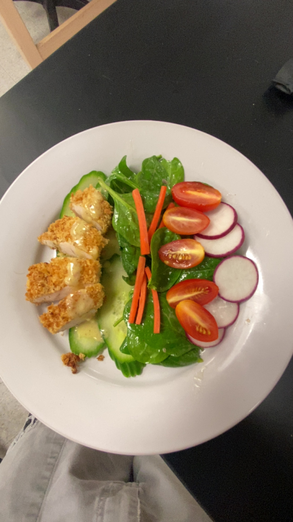 Plate with fried chicken pieces, lettuce, cucumber, cherry tomatoes, and sliced radishes, garnished with carrot sticks.