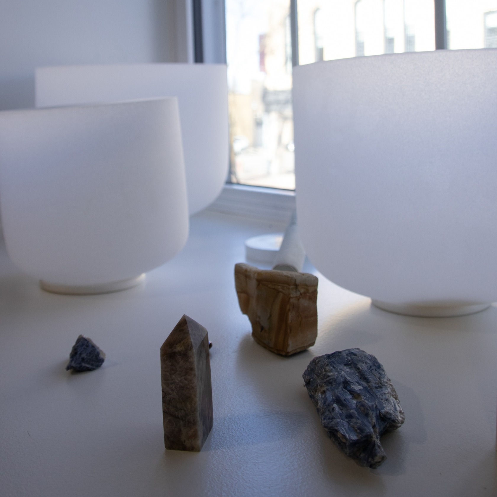 Four rocks on a white surface near a window with white bowls in the background.