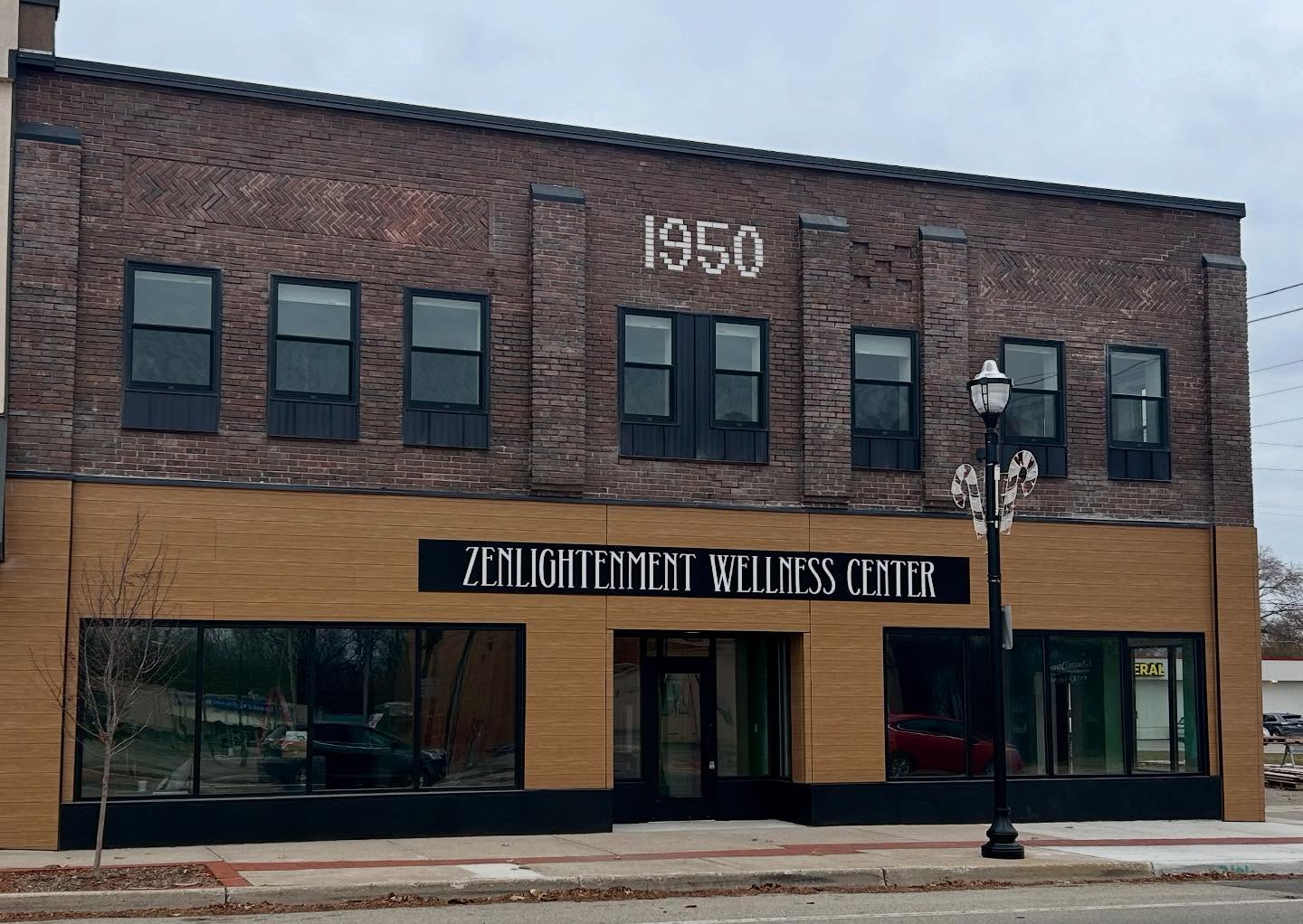 Two-story brick building with a sign for Zenlighenment Wellness Center, large windows, and a streetlamp in front.