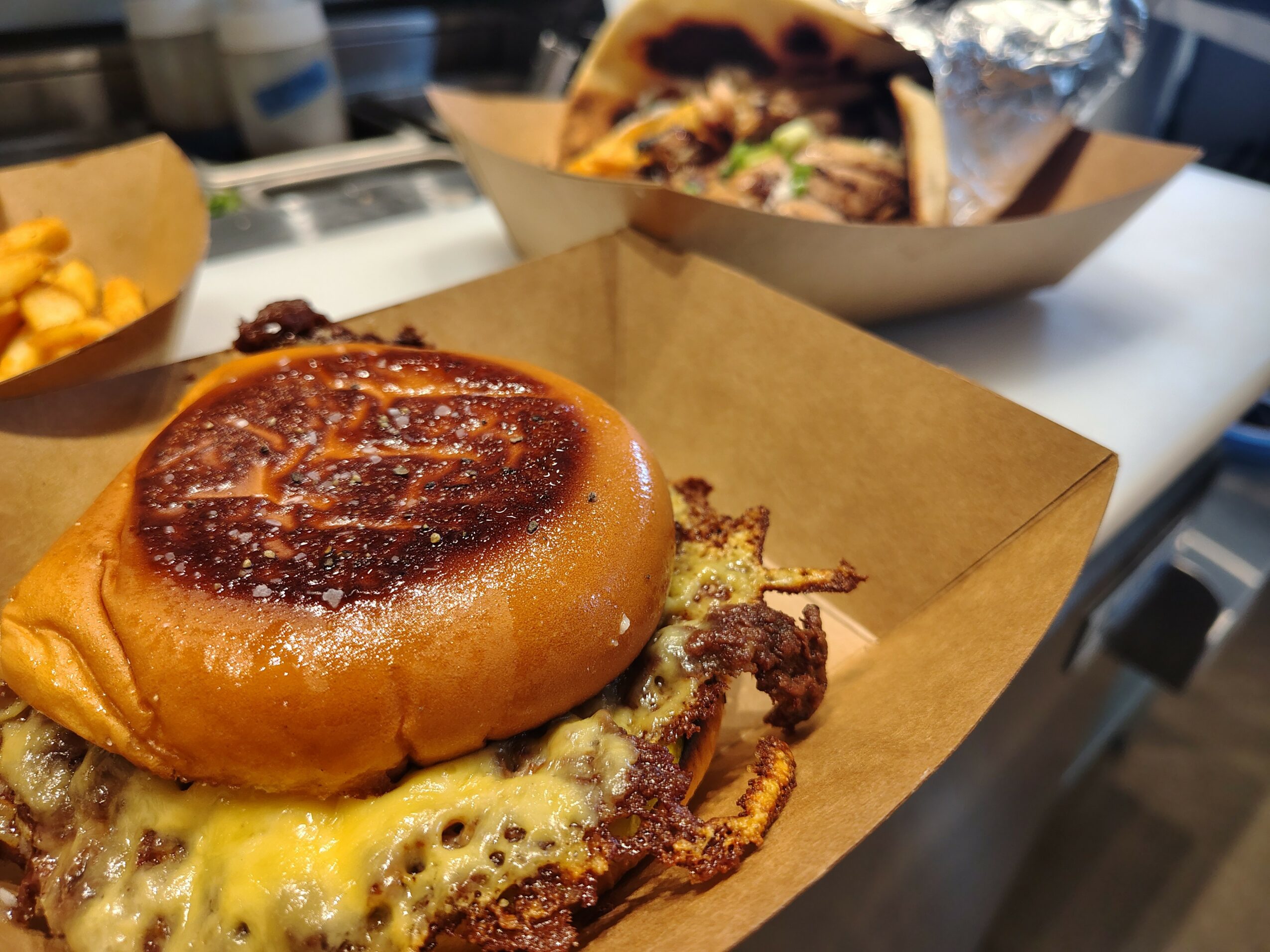 Close-up of a burger with a toasted bun, melted cheese, and meat patty on a paper tray.