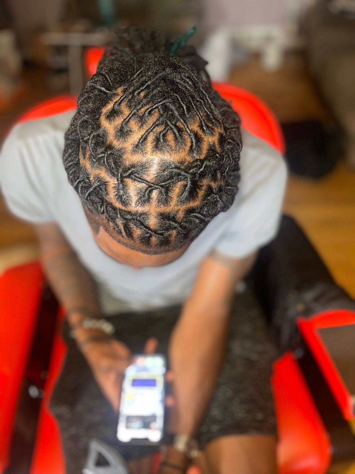 Top view of a person with braided hairstyle, sitting on a red chair, using a smartphone.