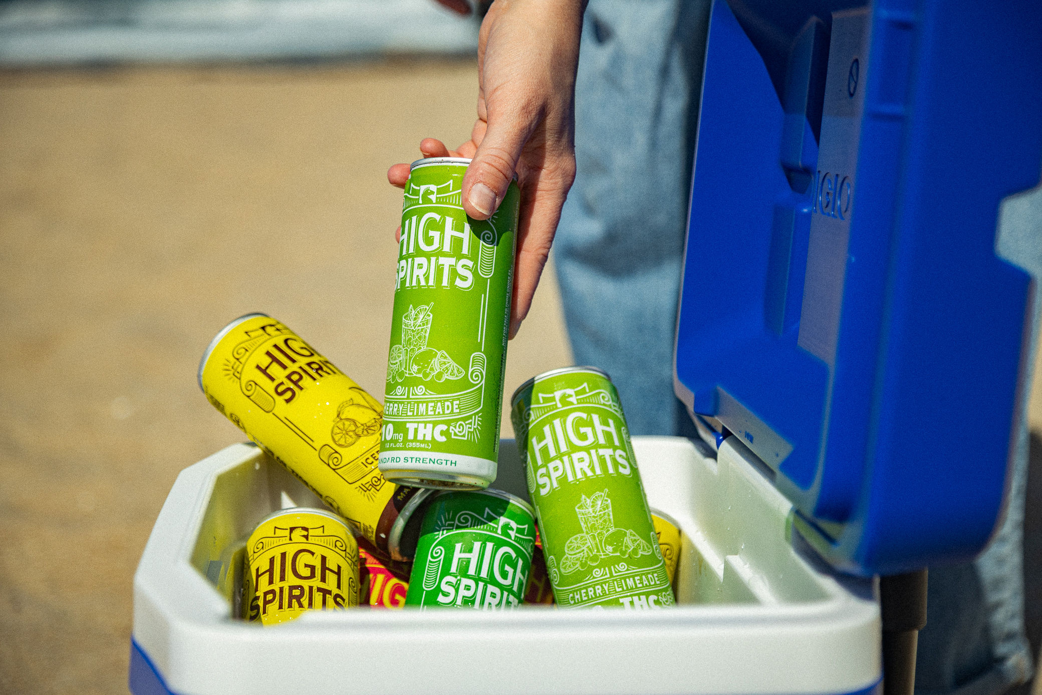 Person's hand reaching into a cooler filled with canned drinks labeled 'High Spirits' and 'Hershey's'.