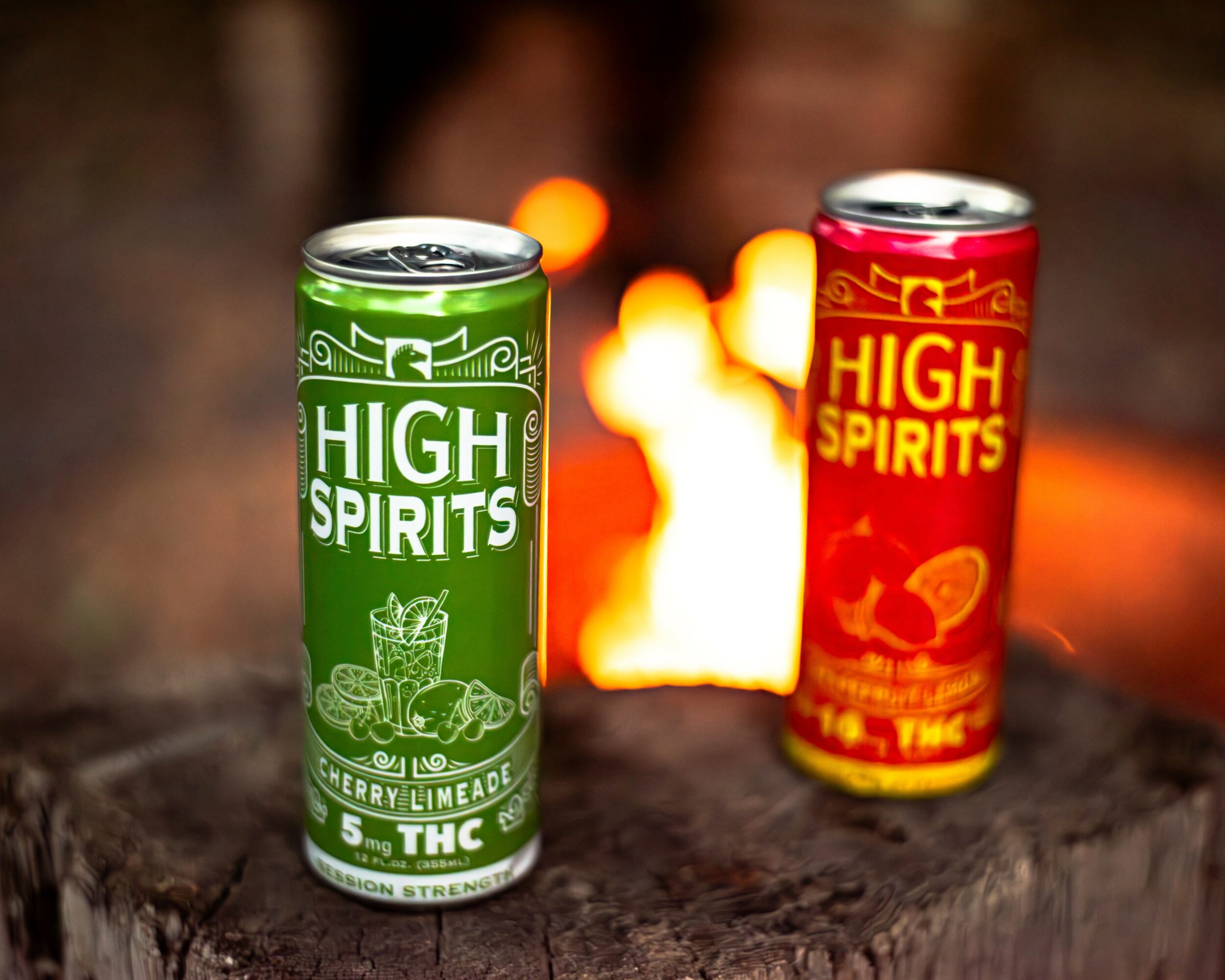 Two cans labeled 'High Spirits' on a wooden surface with a blurred fire in the background.