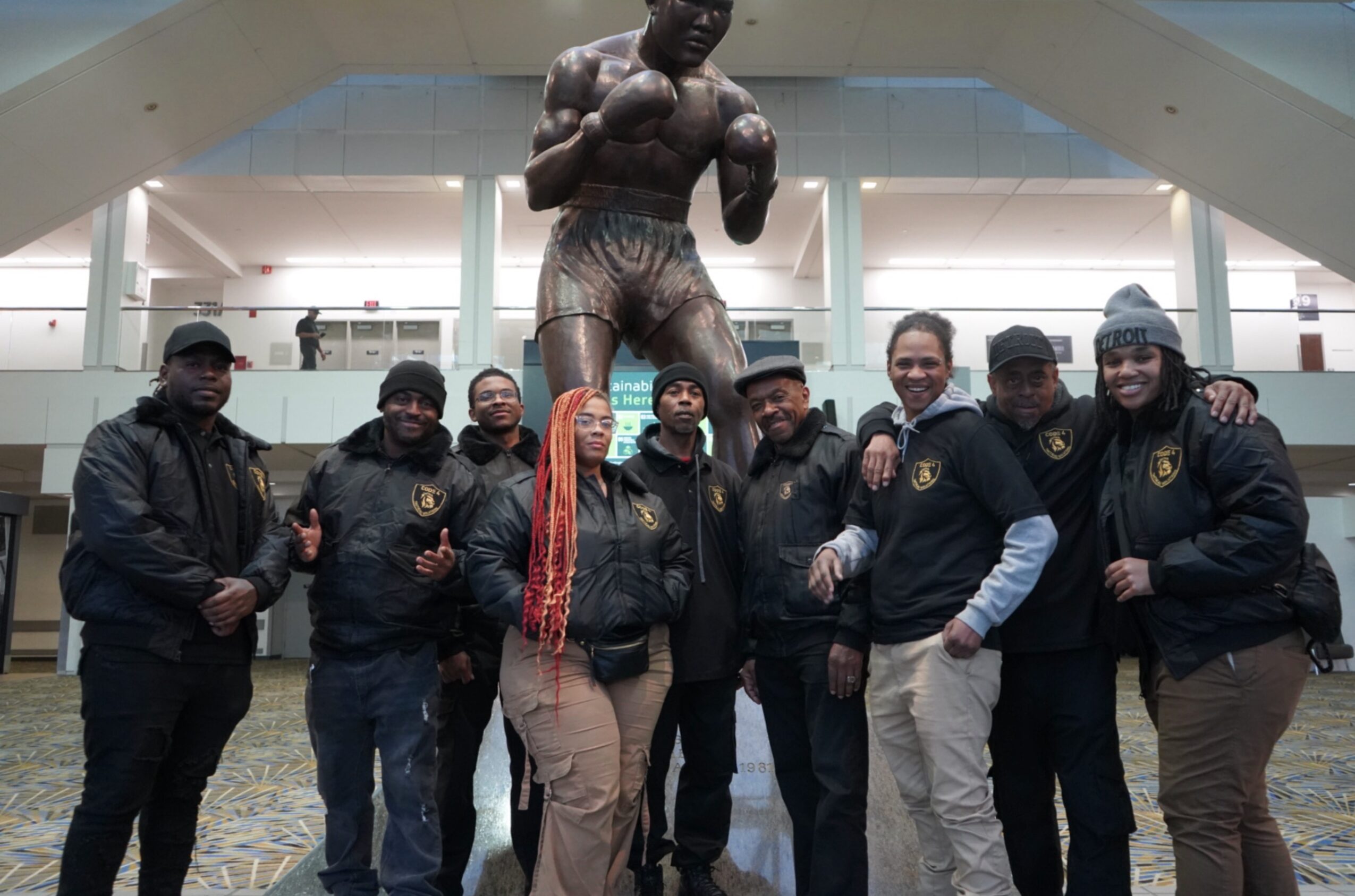 Group of eight people standing in front of a large boxing statue inside a building.