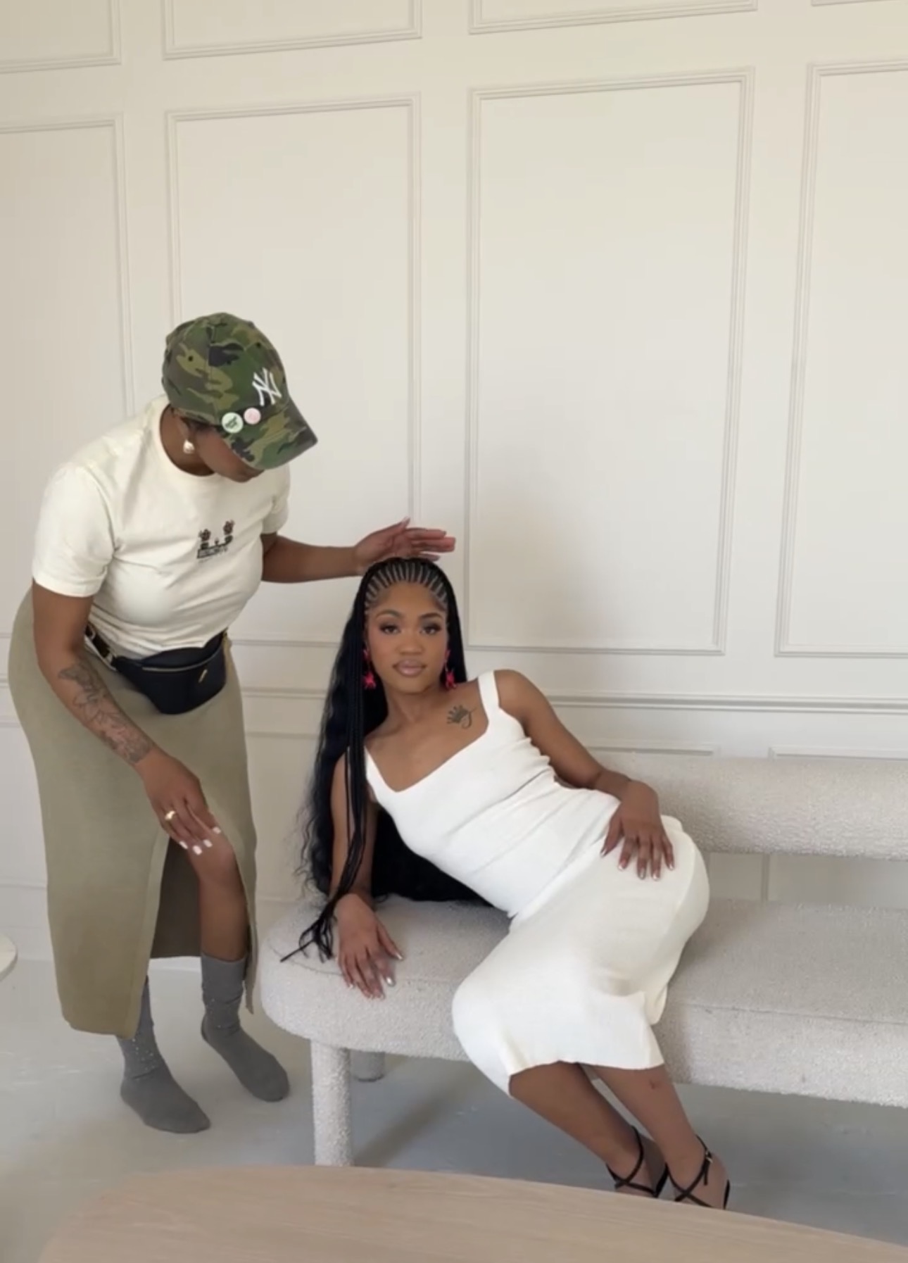 Two women, one sitting on a bench and the other standing beside her, in a room with white paneled walls.