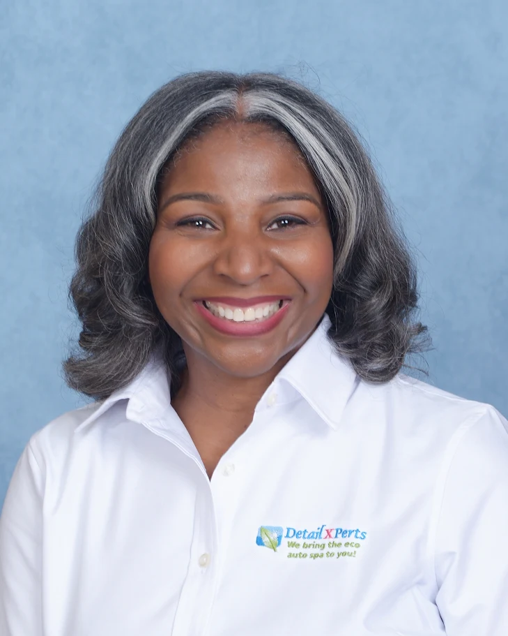 Smiling woman with shoulder-length gray and black hair, wearing a white collared shirt, against a blue background.