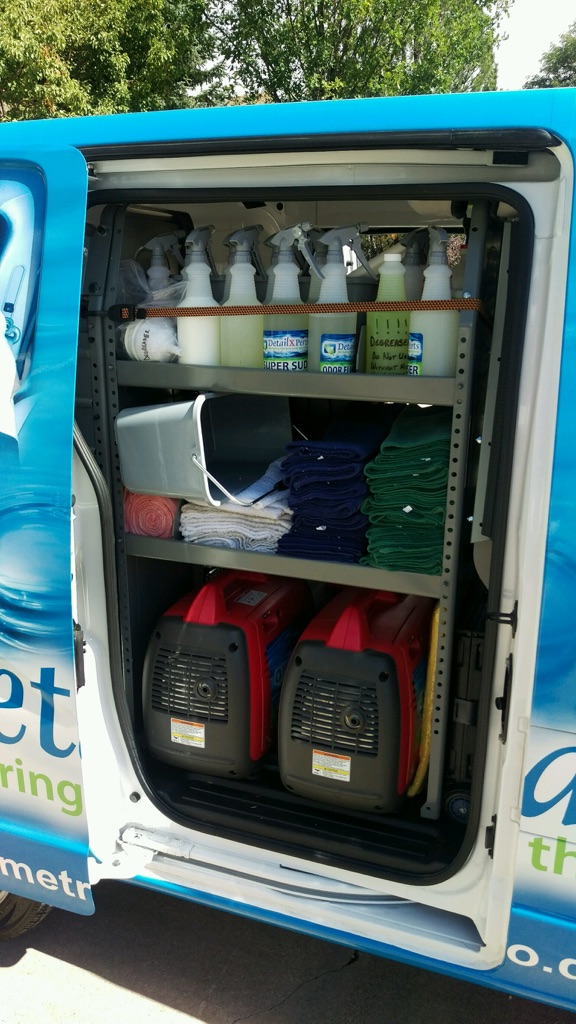 Open vehicle door showing shelves with spray bottles, cleaning supplies, and red containers inside the vehicle.