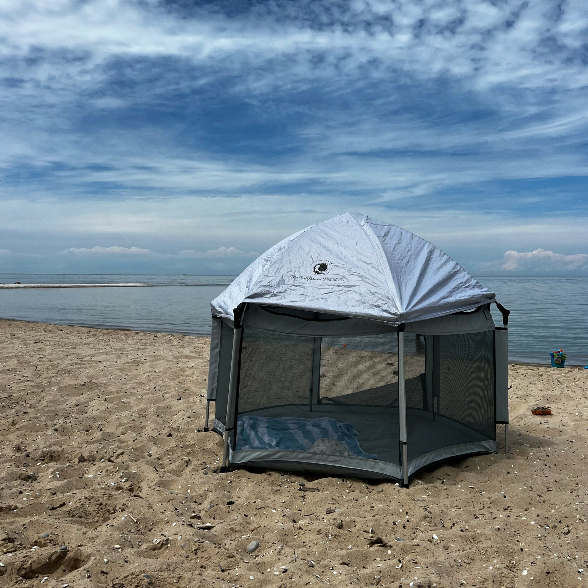 Beach scene with a white pop-up tent on sandy shore, ocean and sky with clouds in background.