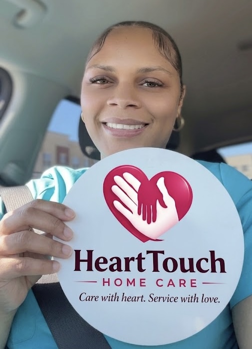 Woman smiling holding a circular sign with a heart and hand logo, and text about home care services.