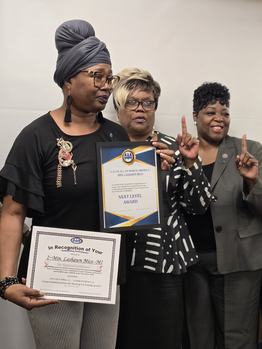 Three women standing together, one holding a certificate, smiling and making peace signs, in an indoor setting.