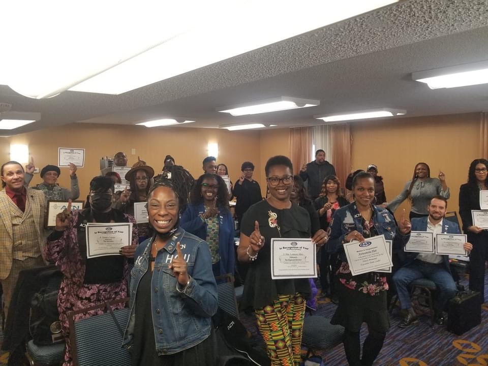 Group of people holding certificates, smiling, in a room with wooden walls and ceiling lights.