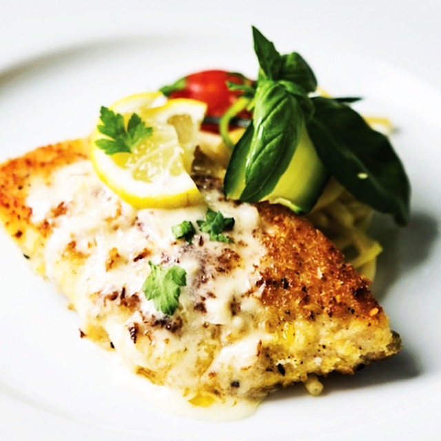 Baked fish fillet with lemon slices, cherry tomatoes, and fresh basil on a white plate.