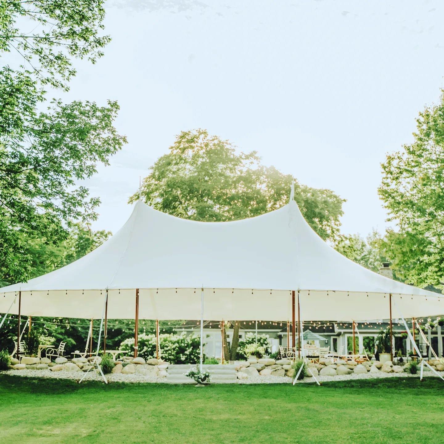 Large white tent set up outdoors with trees and a grassy area, under a clear sky.