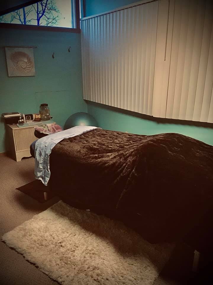 Bedroom with bed, nightstand, and window with blinds, illuminated by natural light, with a rug on the floor.