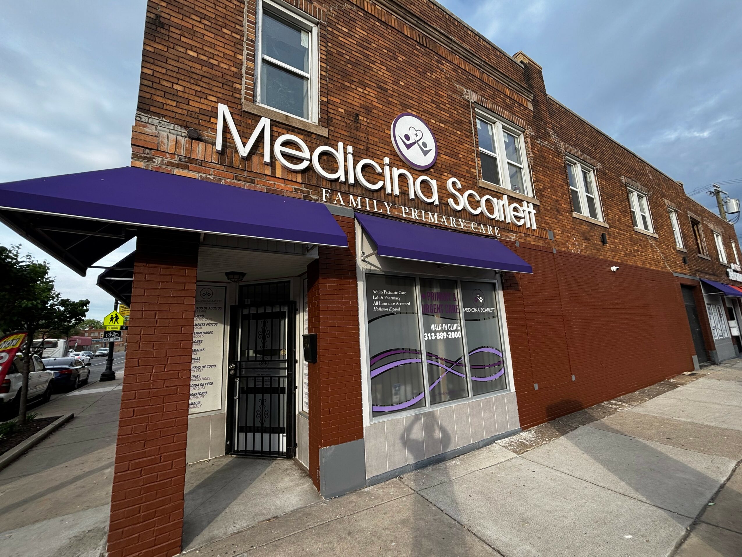 Brick building with a purple awning and signage for Medicina Scarlett Family Eyecare, with windows and sidewalk in front.