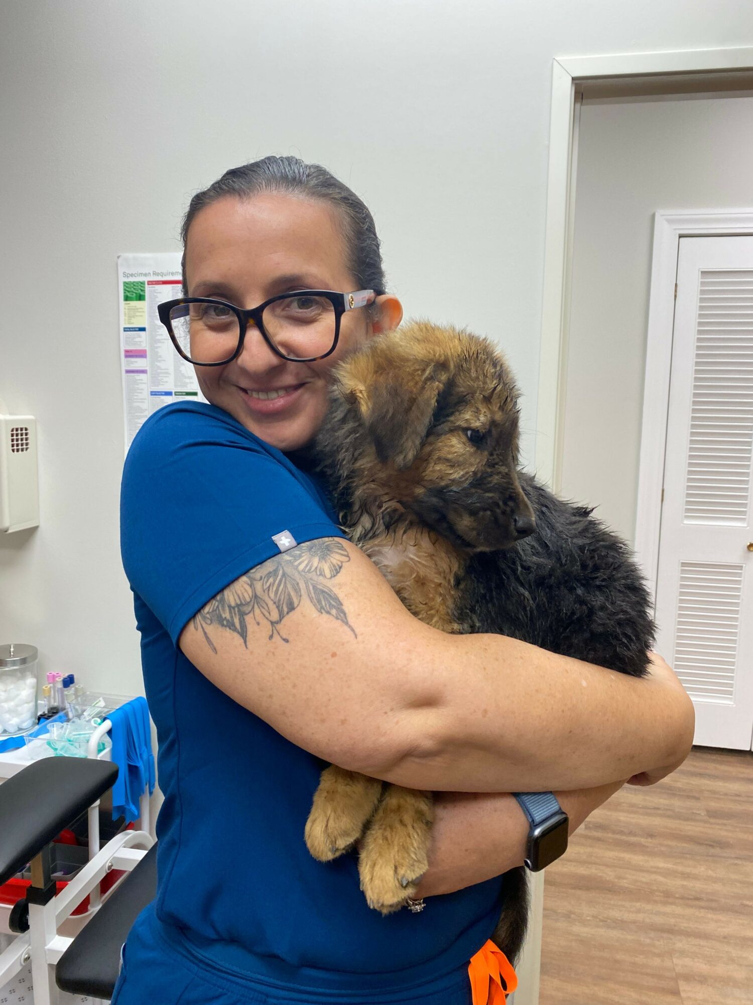 Woman with glasses holding a fluffy puppy indoors, smiling at the camera.
