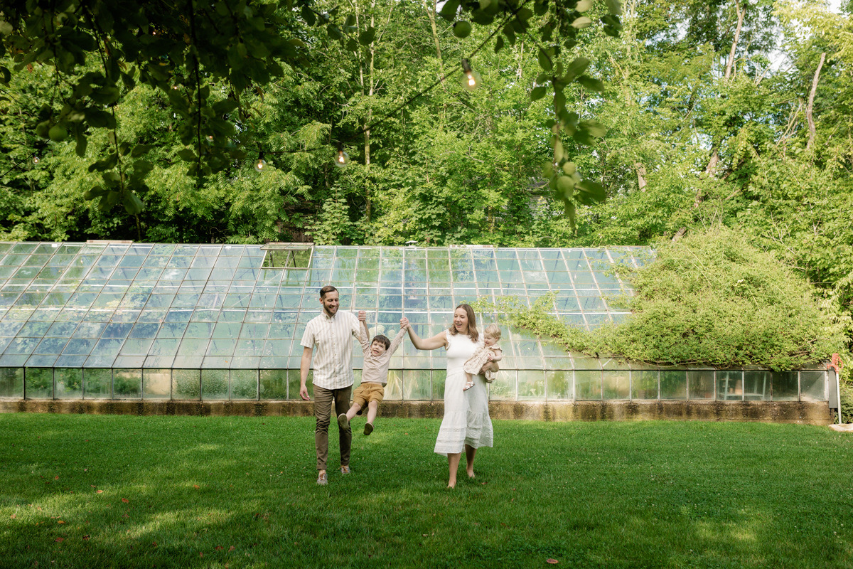 Three people standing on grass in front of a greenhouse with trees in the background.