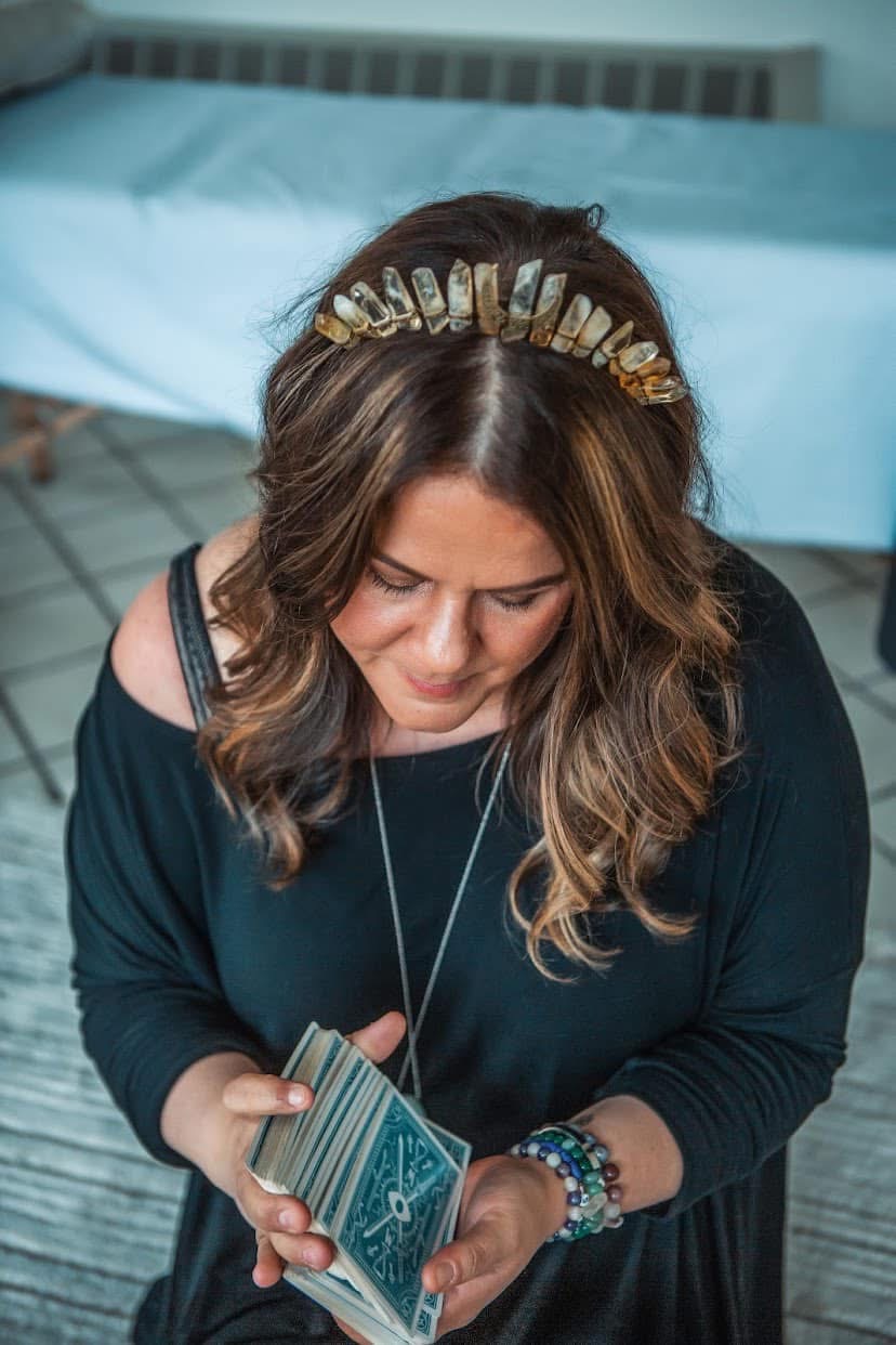 Woman with wavy hair wearing a headband, looking down at her phone, in a room with a bed and tiled floor.