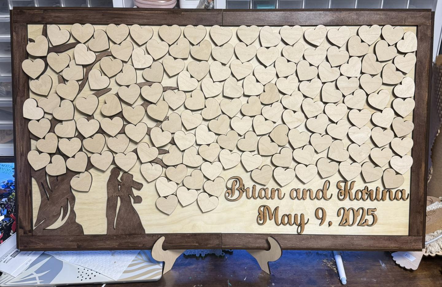 Wooden display with heart-shaped cutouts, silhouette of a couple, and personalized text with names and date.