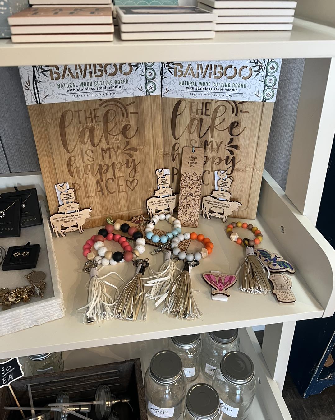 Three beaded and tassel keychains with colorful beads and charms on a white shelf, with decorative signs behind them.