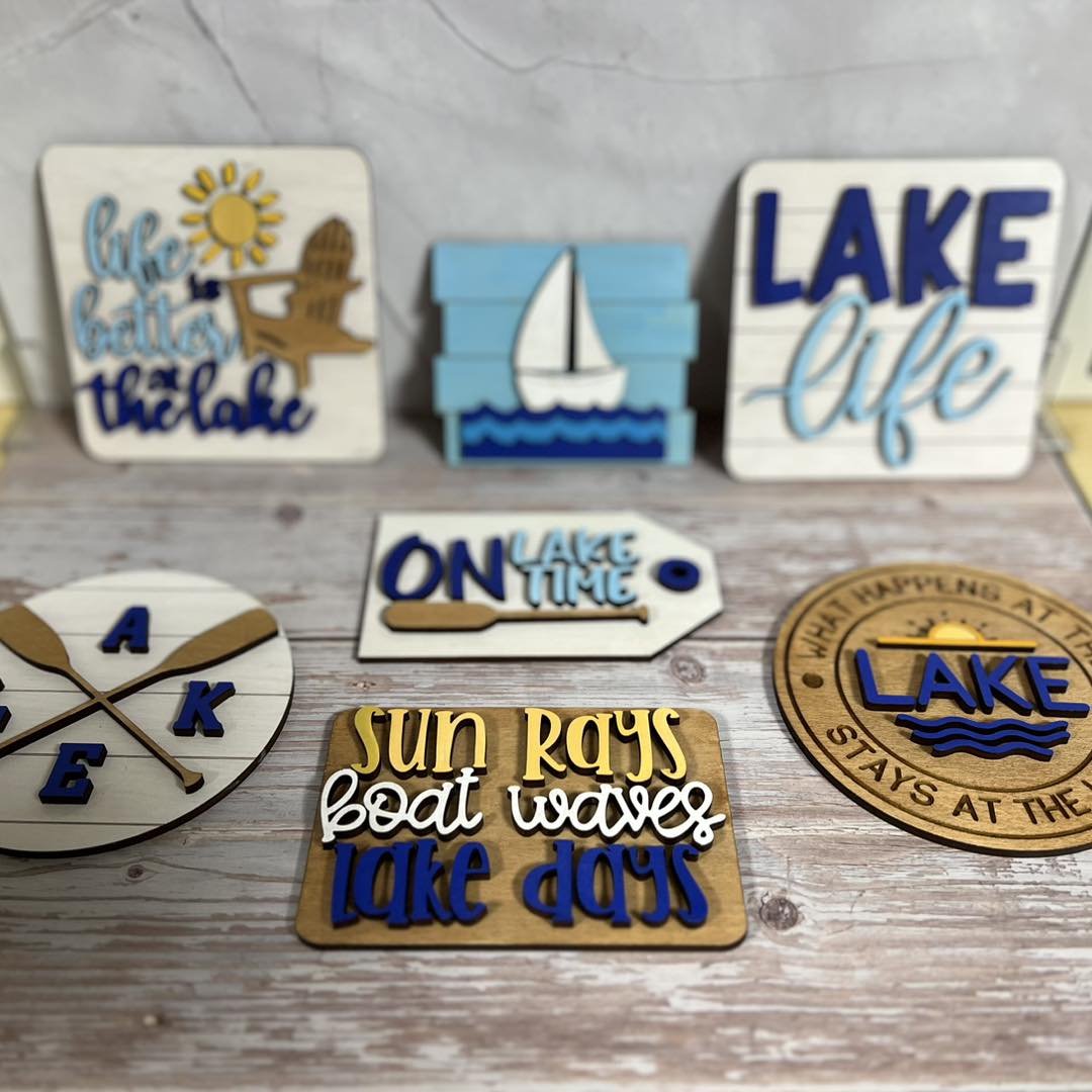 Six decorative items with lake and boat themes, including signs and a clock, arranged on a wooden surface.