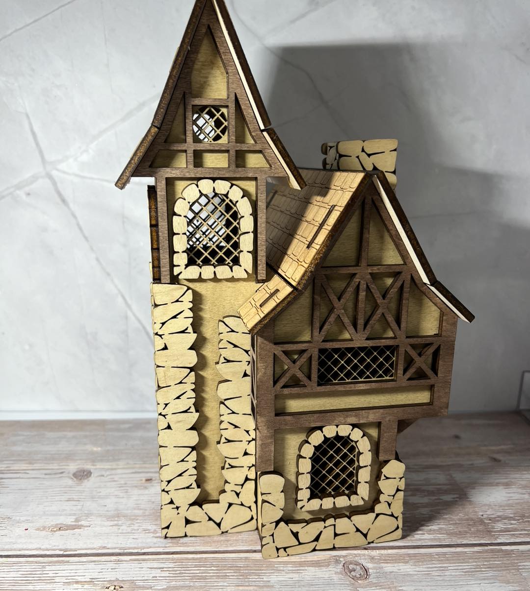 Wooden miniature house with multiple towers, detailed windows, and stone-like base, placed on a wooden surface.