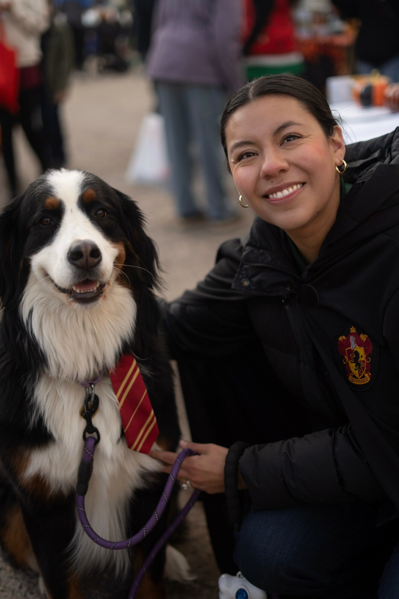 Woman smiling with a black and white dog wearing a striped tie, outdoors at an event.