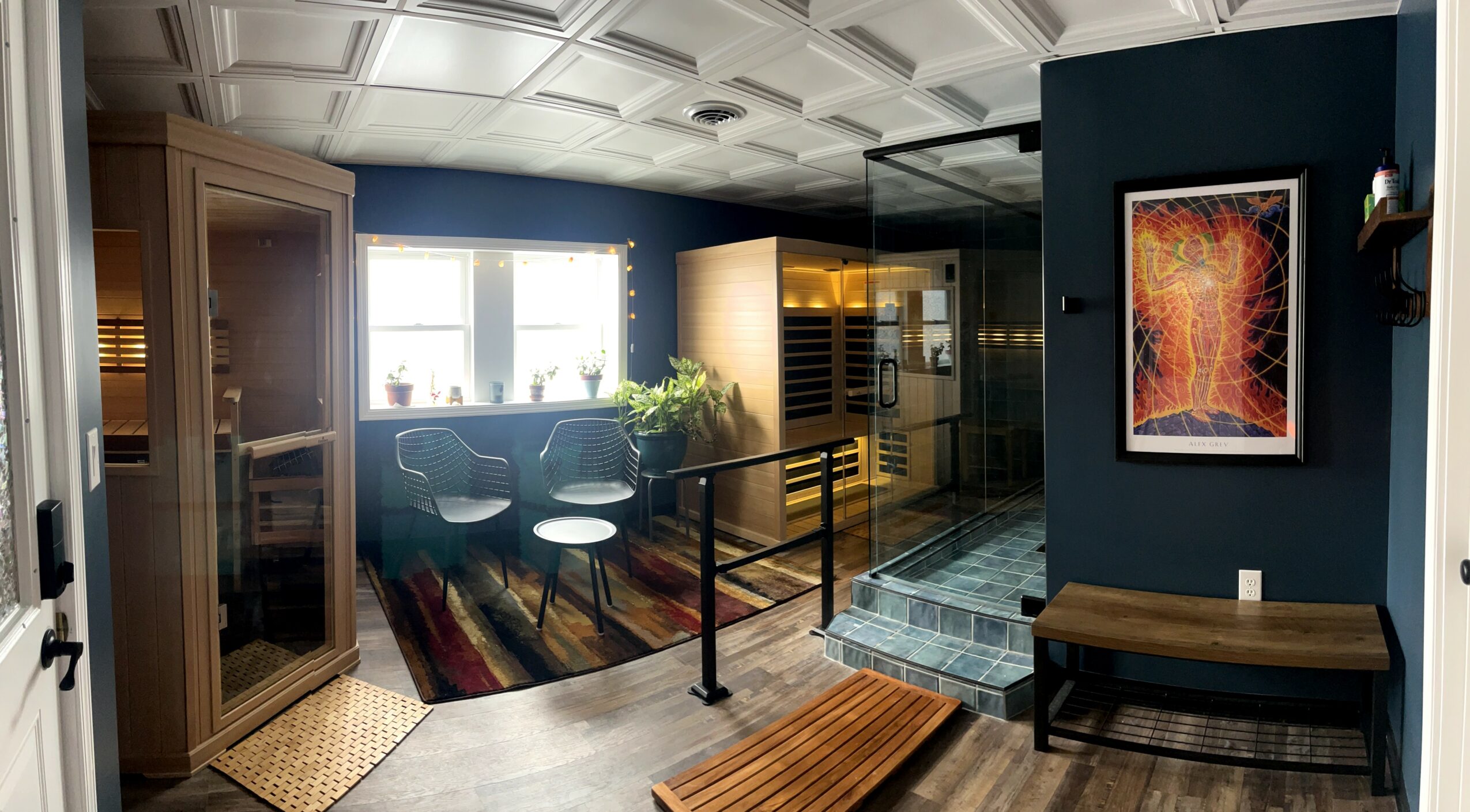 Interior view of a modern room with artwork, a bench, a glass staircase, and a seating area with windows.