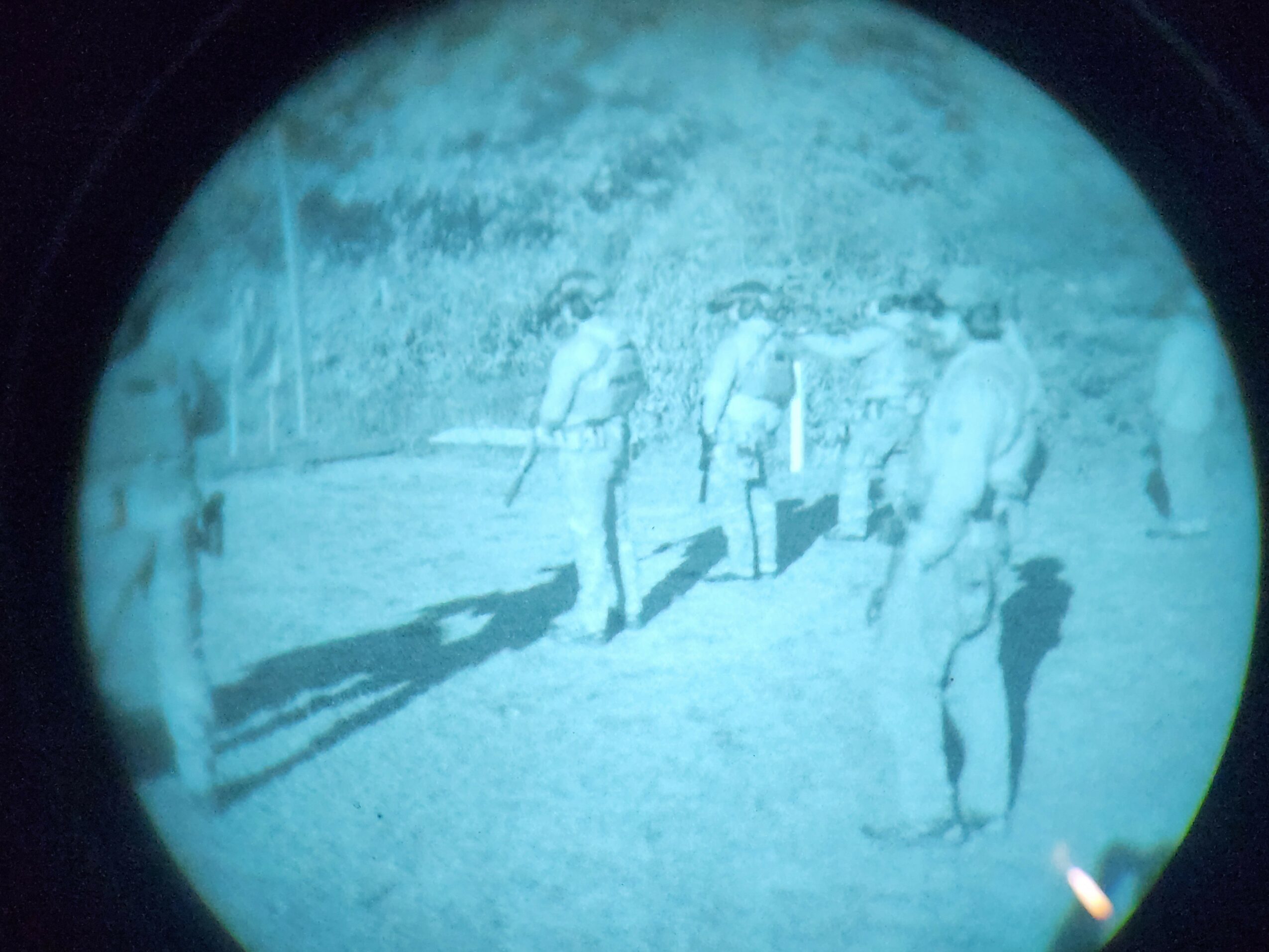 Group of people walking outdoors, some wearing hats, with trees and a fence in the background.