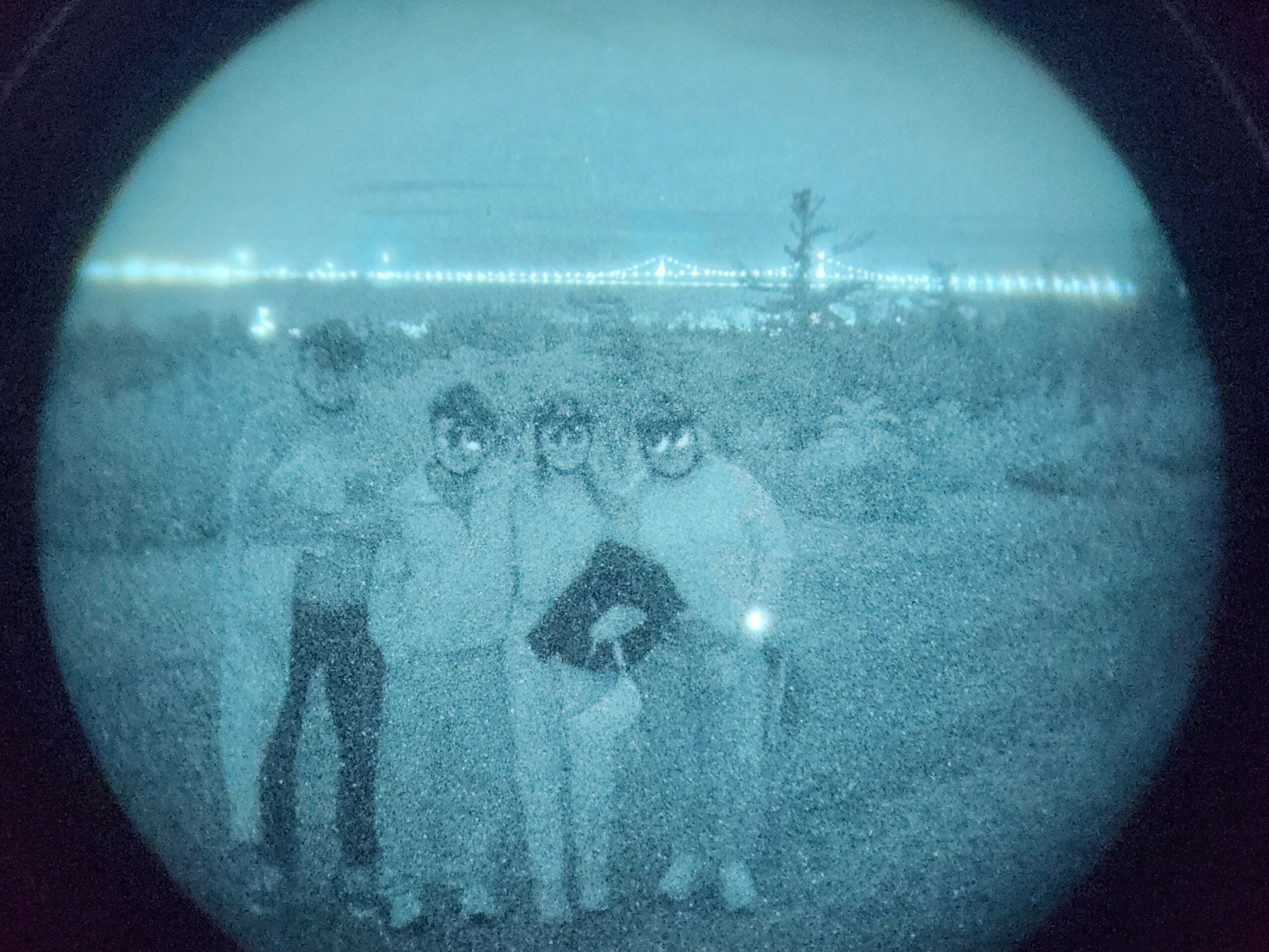 Four people standing outdoors in a field, with a tree and power lines in the background, viewed through a circular lens.