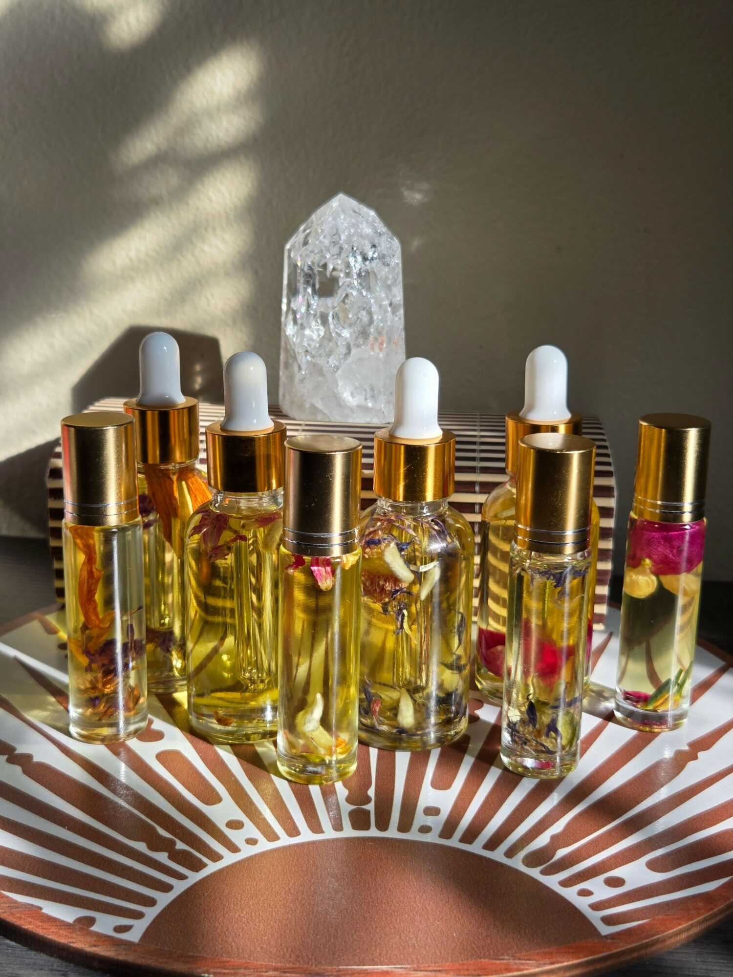 Collection of small glass bottles with golden caps, some with pink and red flower petals inside, arranged on a decorative surface.