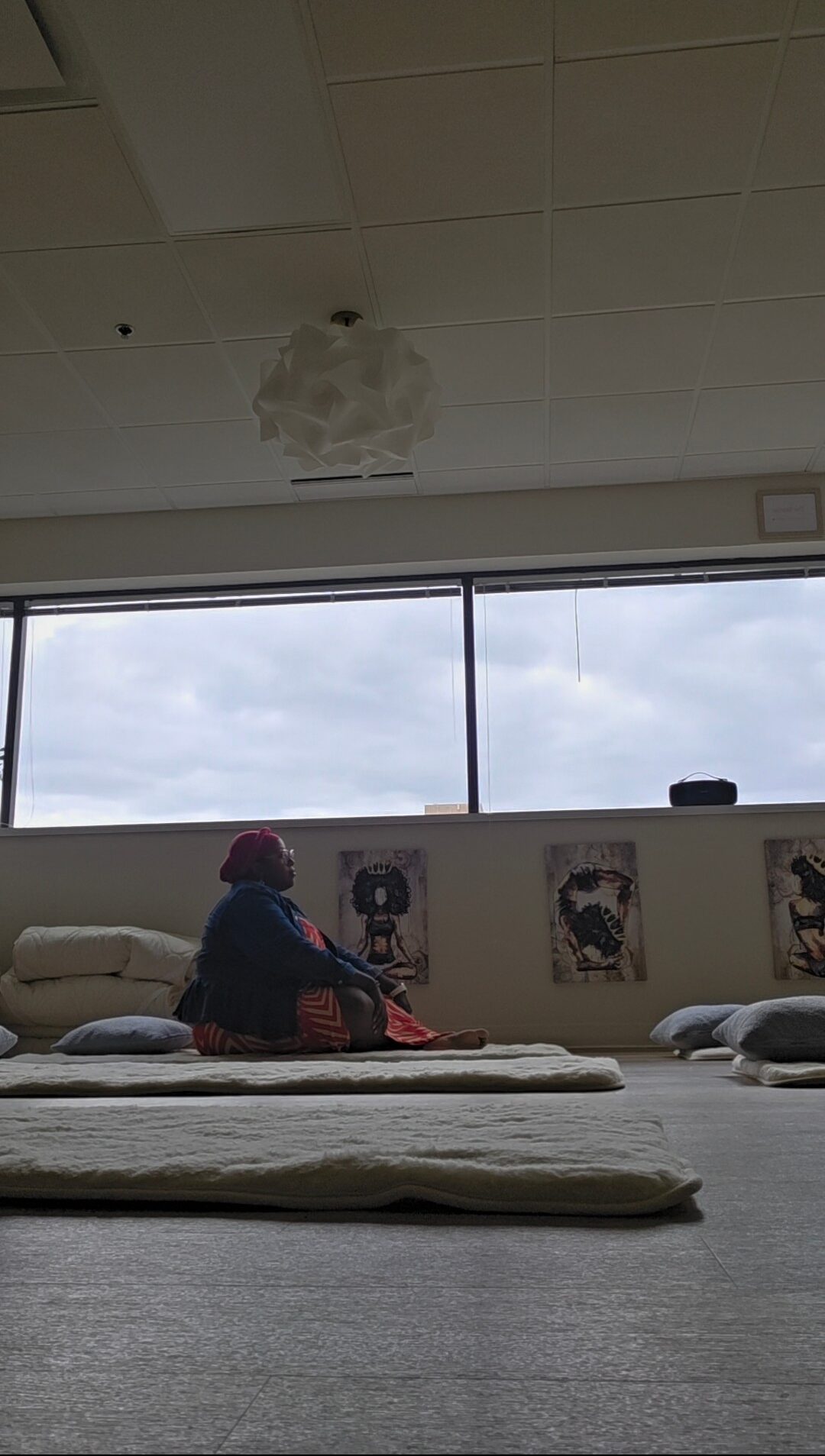 Person sitting on the floor near a window, with posters on the wall and a ceiling with a damaged area.