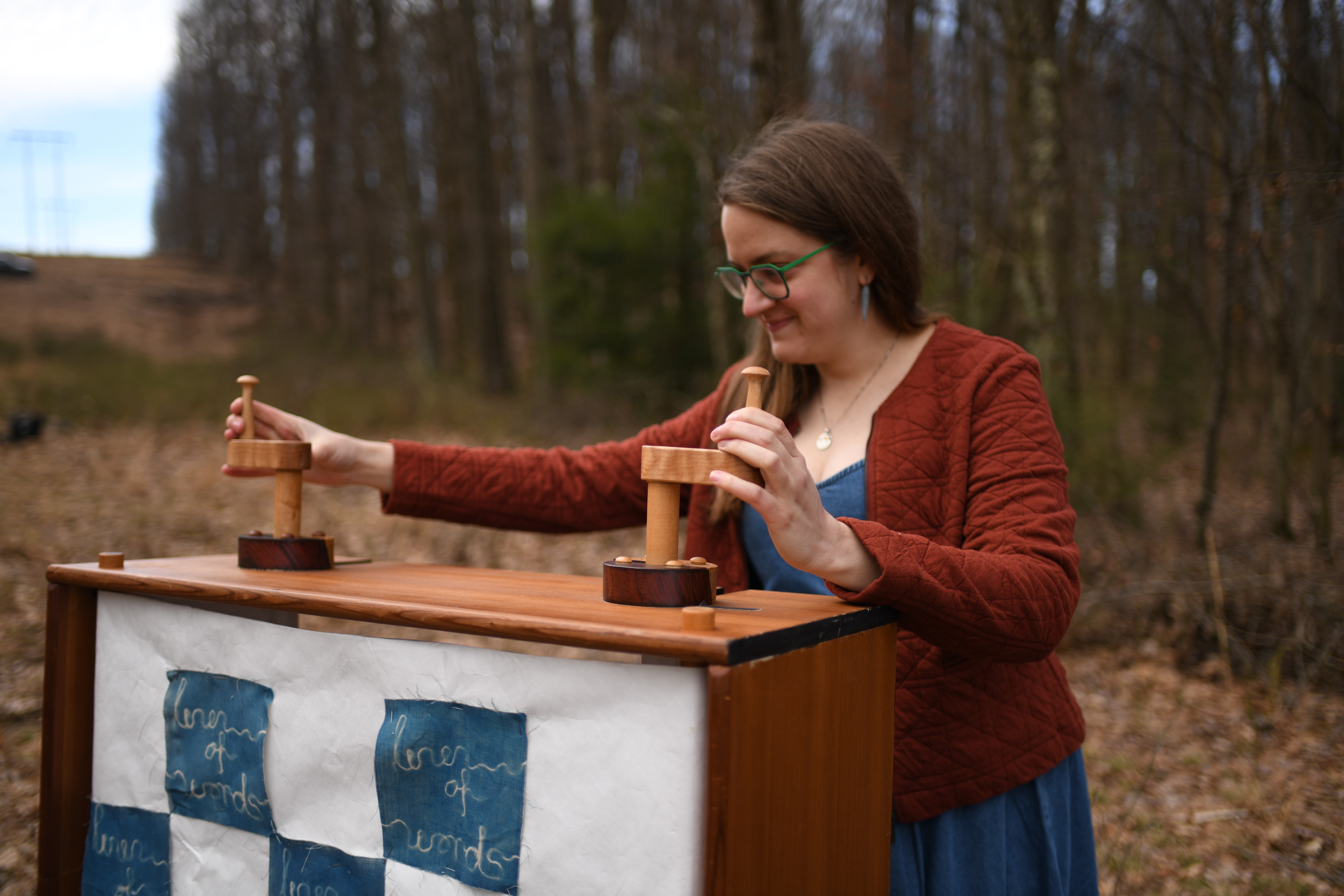Woman with glasses and brown hair playing chess outdoors in a forested area.