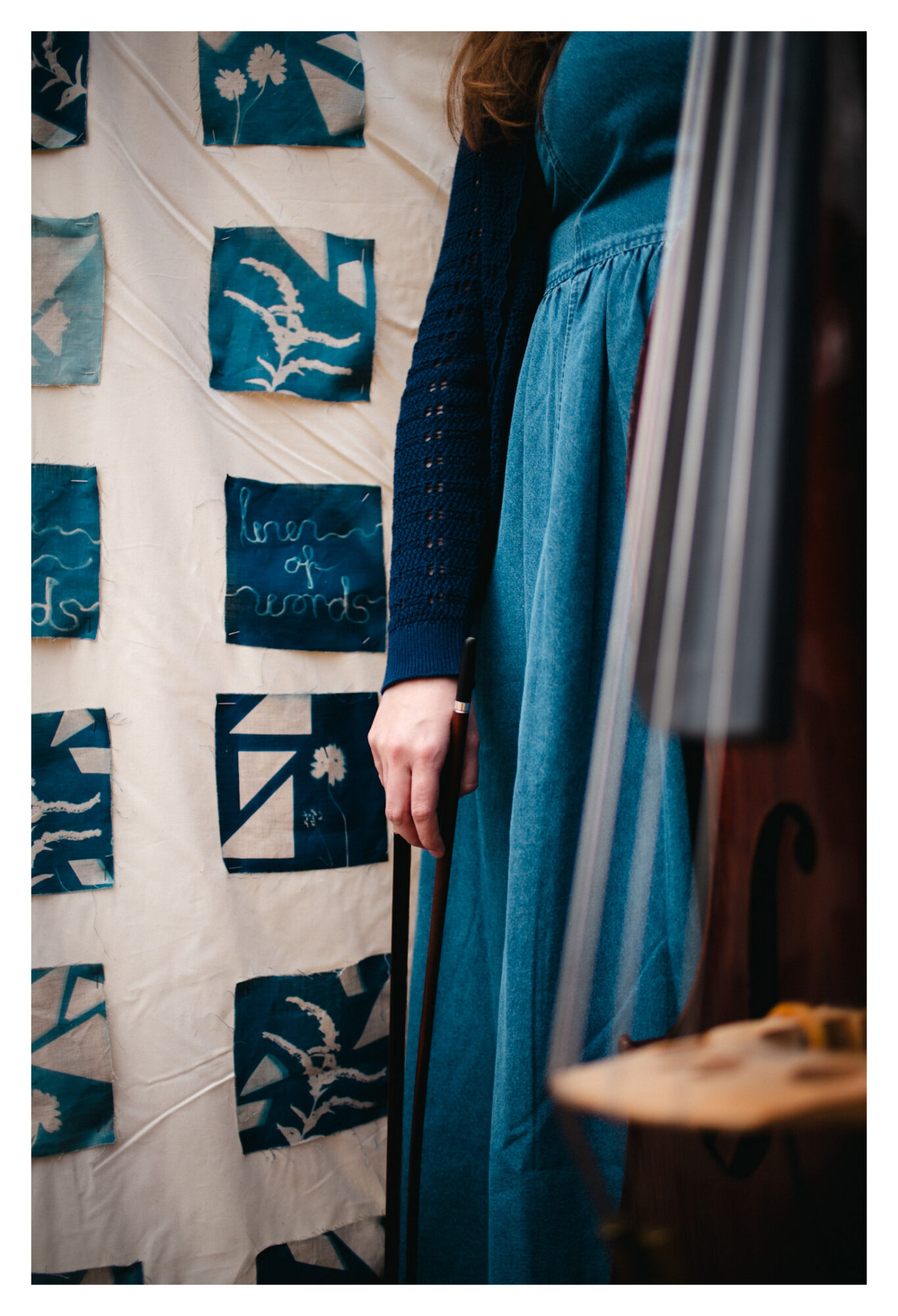 Person wearing a blue dress and black cardigan standing near a wall with blue and white artwork.