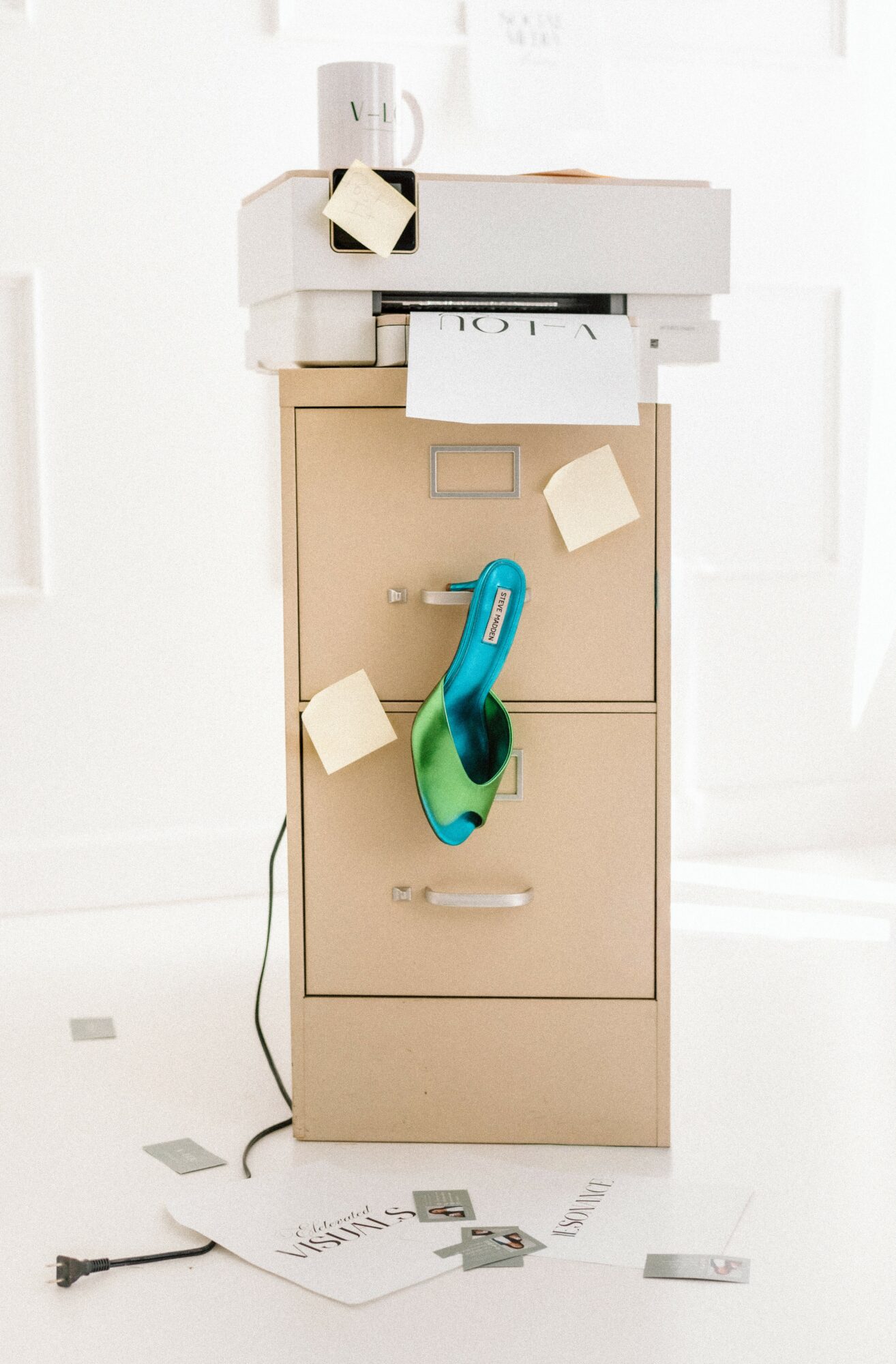 A beige filing cabinet with papers and sticky notes attached, topped with white boxes, in a bright room.