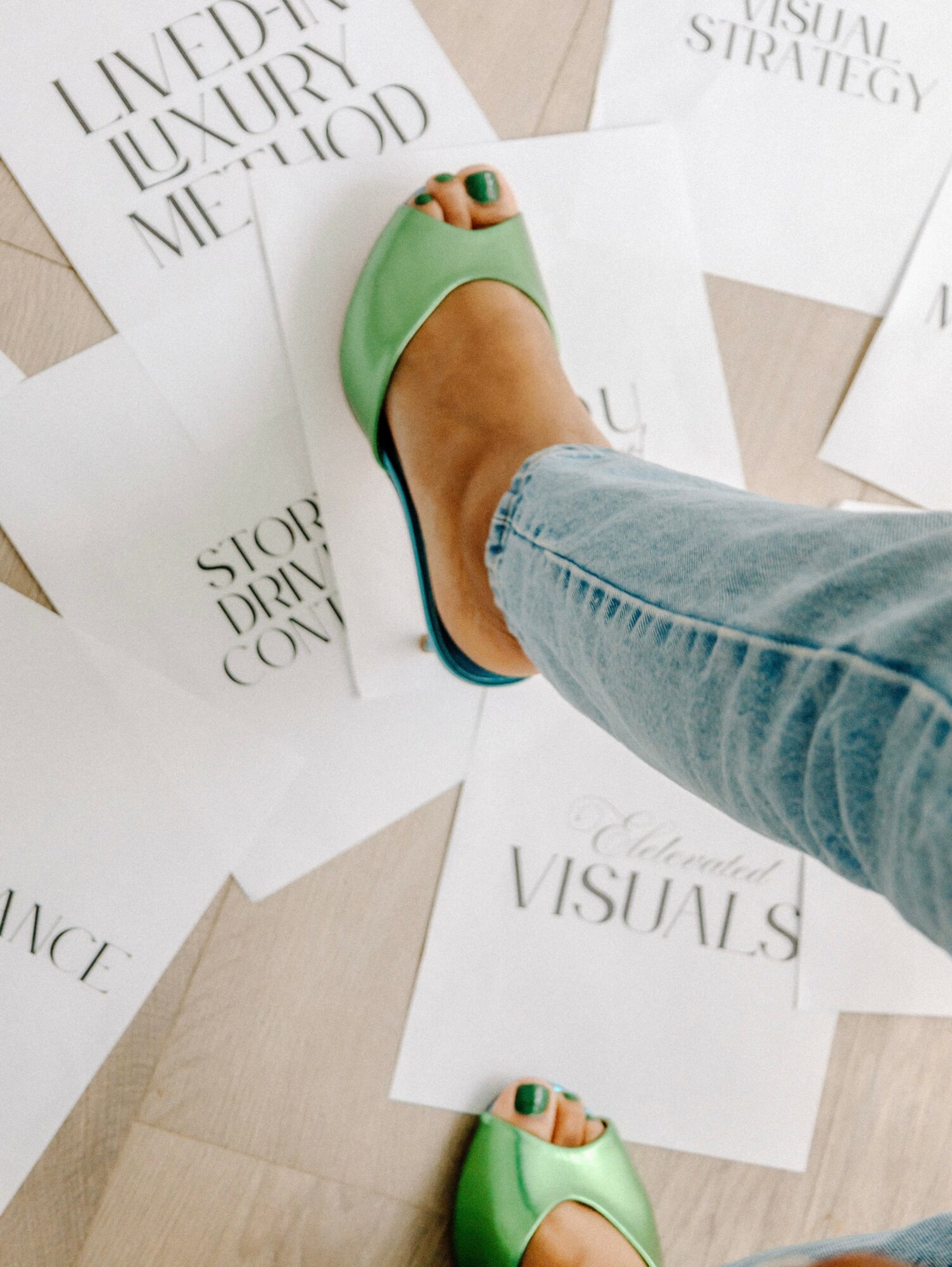 Person wearing green shoes and jeans stepping on scattered papers on the floor.