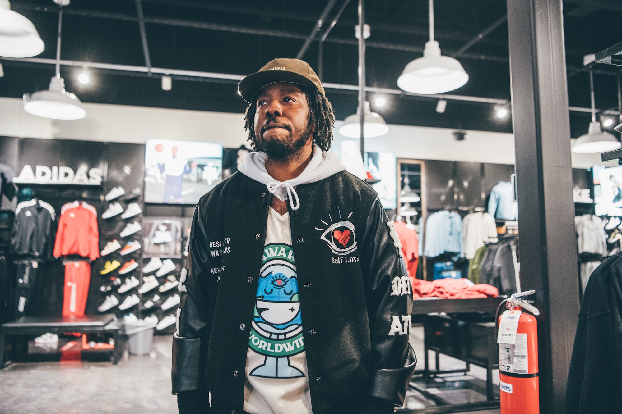 Man with dreadlocks and beard wearing a black jacket and cap inside a clothing store.