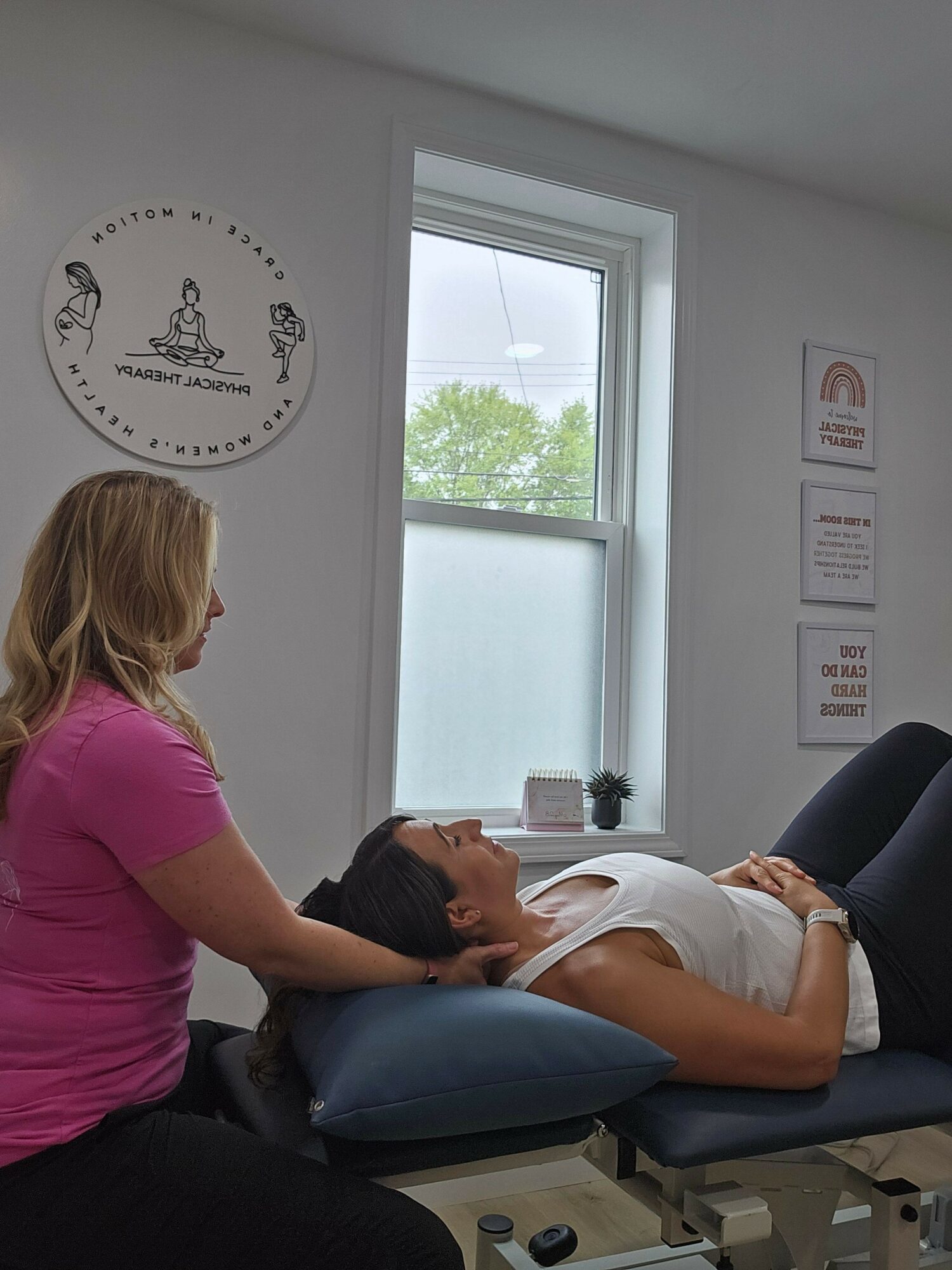 Person lying on a medical examination table with a healthcare professional attending to them, in a clinical room with a window.