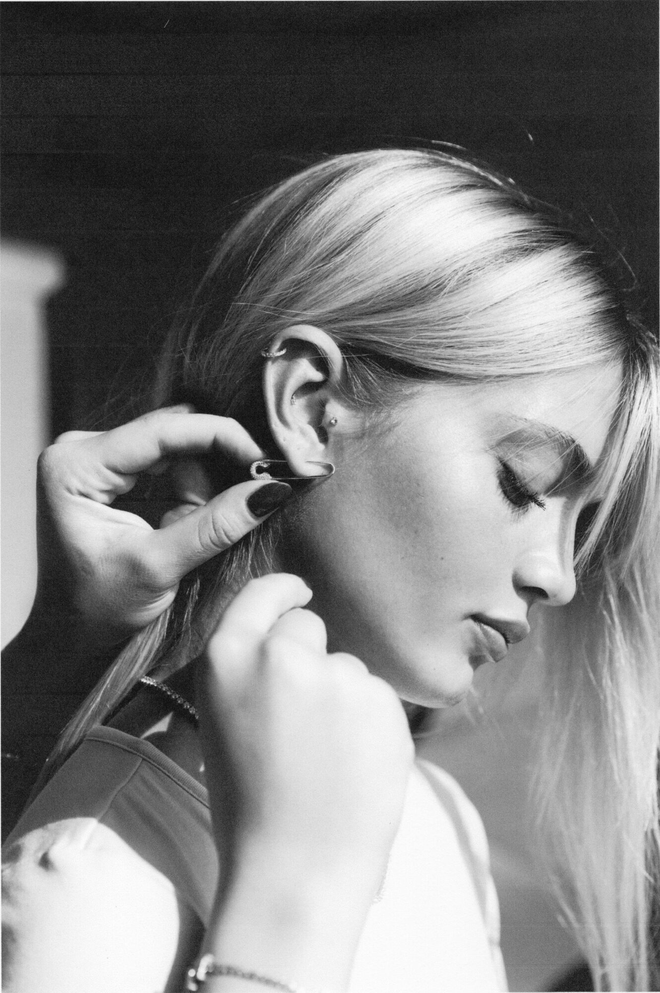 Profile of a woman with closed eyes, adjusting an earring, with long hair and a contemplative expression.