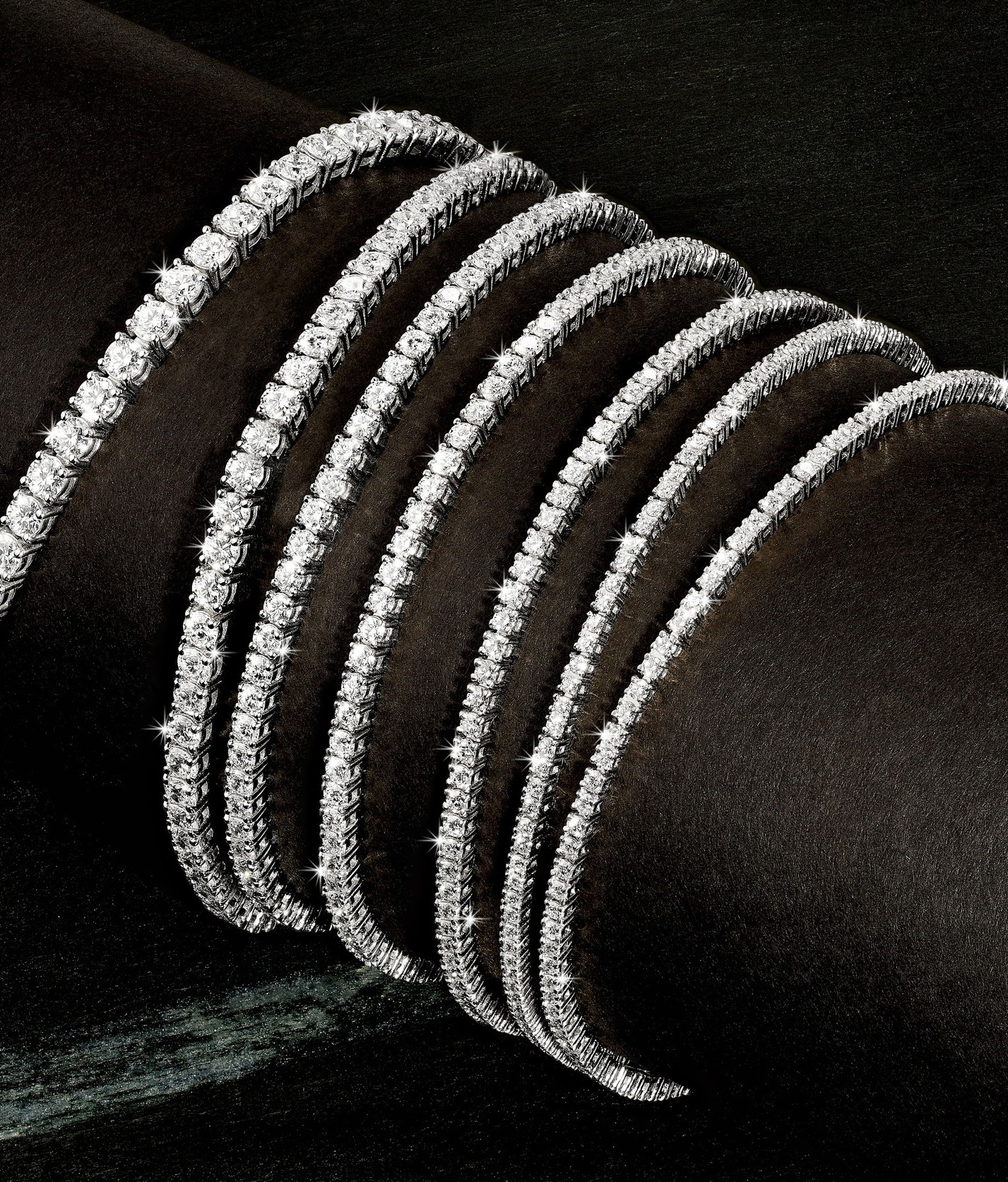 Six diamond-studded bracelets displayed on a dark surface, shiny and reflective, with a close-up view.
