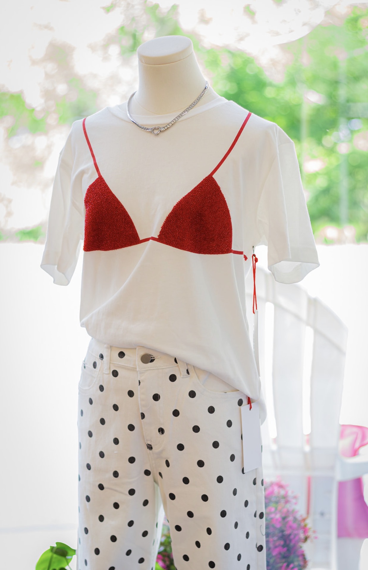 Mannequin wearing a white shirt with red bra top and polka dot pants, outdoors with greenery in background.
