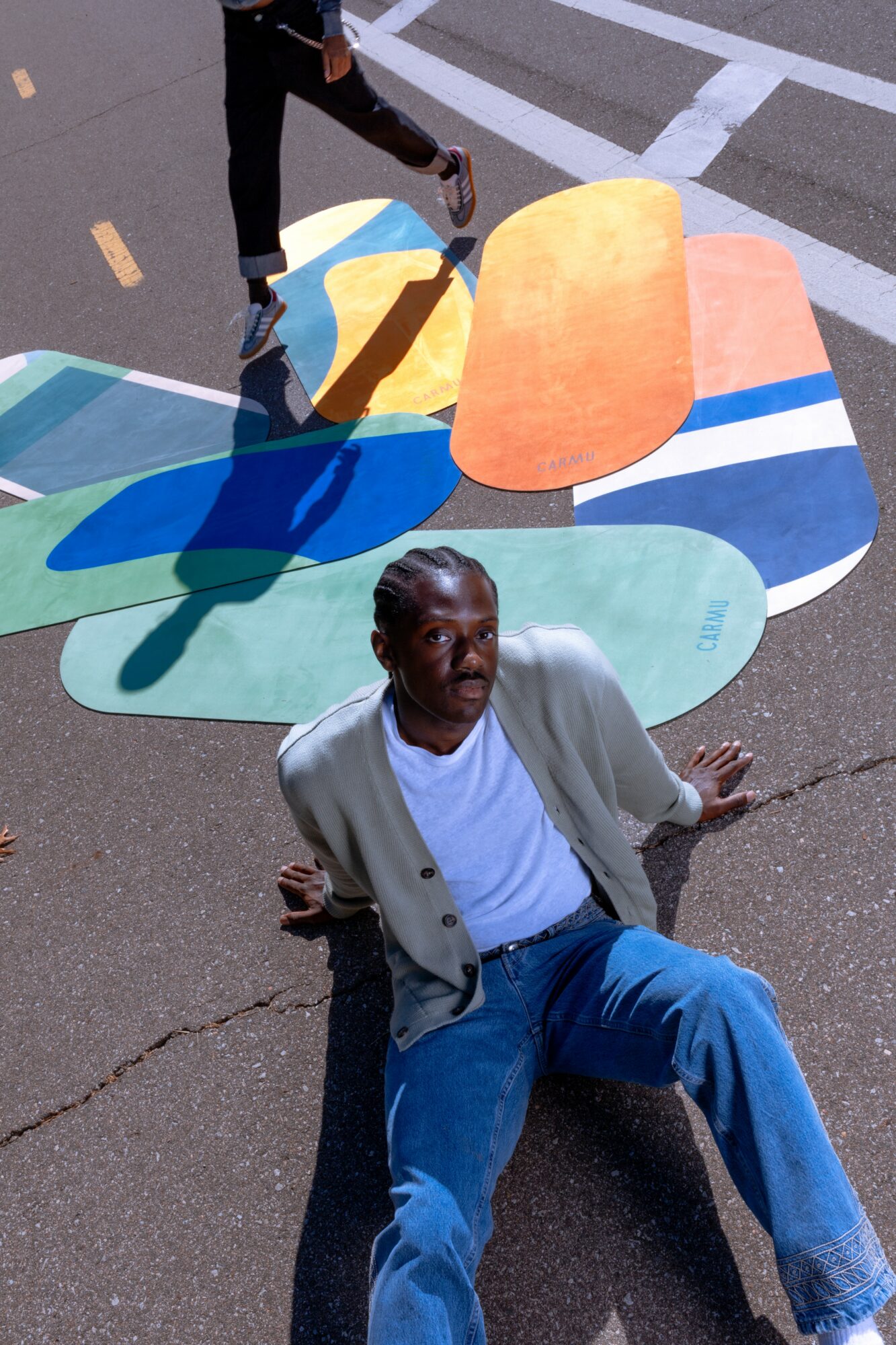 Person sitting on the ground with colorful abstract shapes behind them on a street.