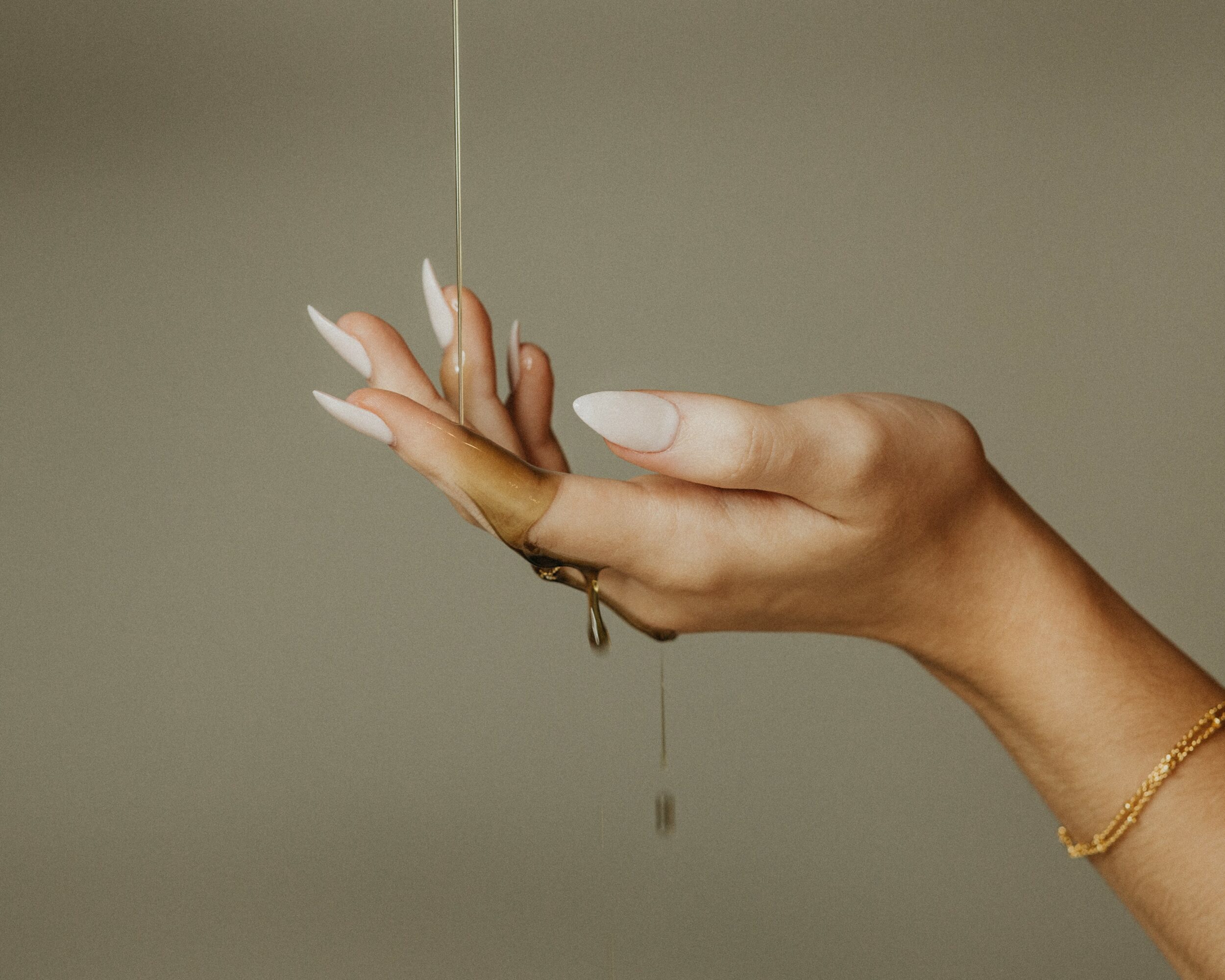 A hand with white nails holds a thin string with a droplet of liquid falling from it.